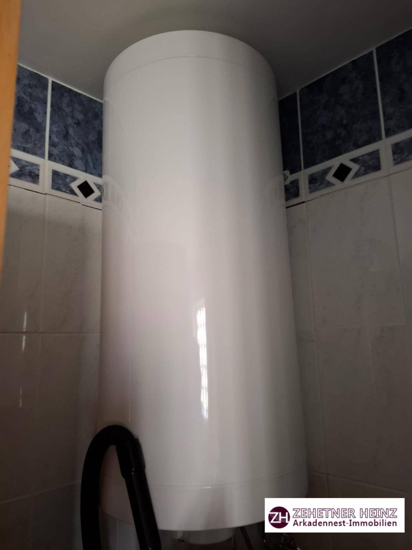 Großer Warmwasserspeicher in einem gefliesten Raum, möglicherweise ein Hauswirtschaftsraum.