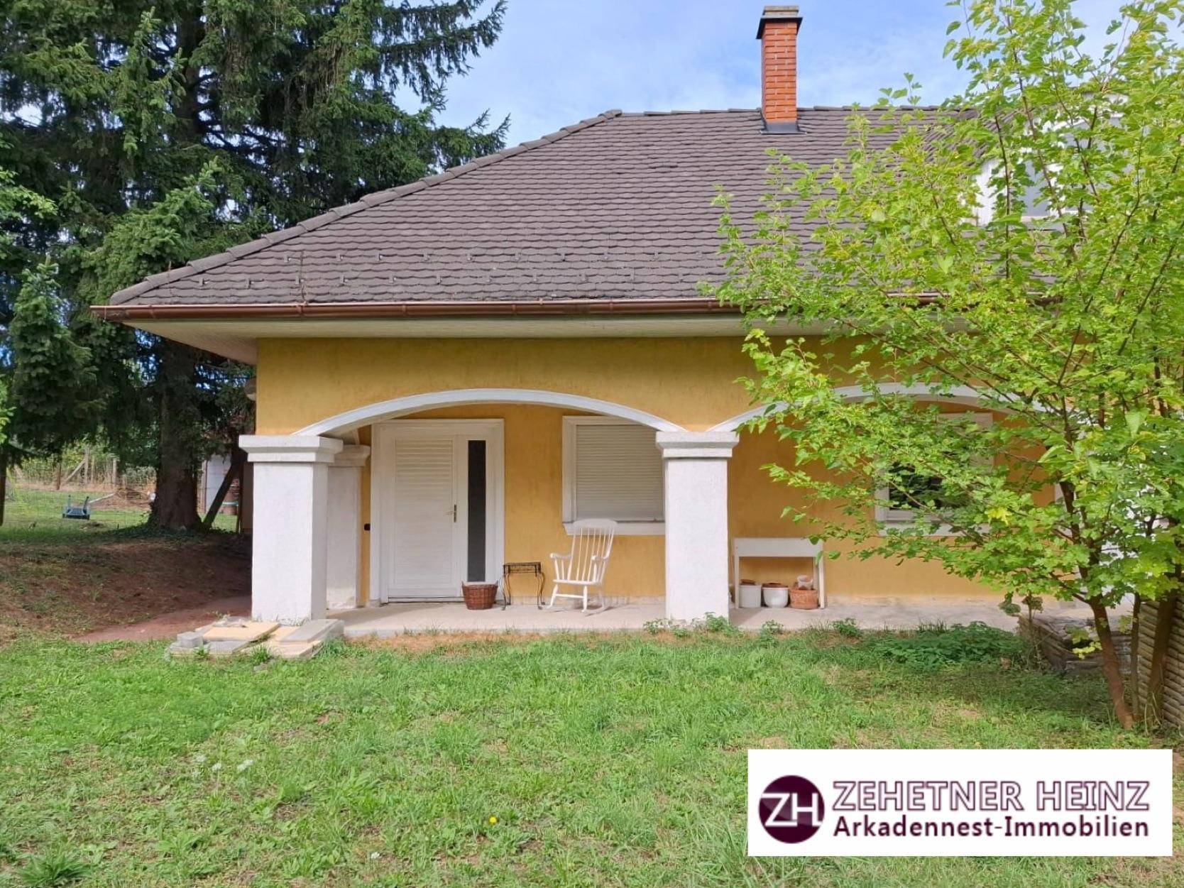 Gelbes Haus mit überdachtem Eingangsbereich und Rasenfläche im Vorgarten.