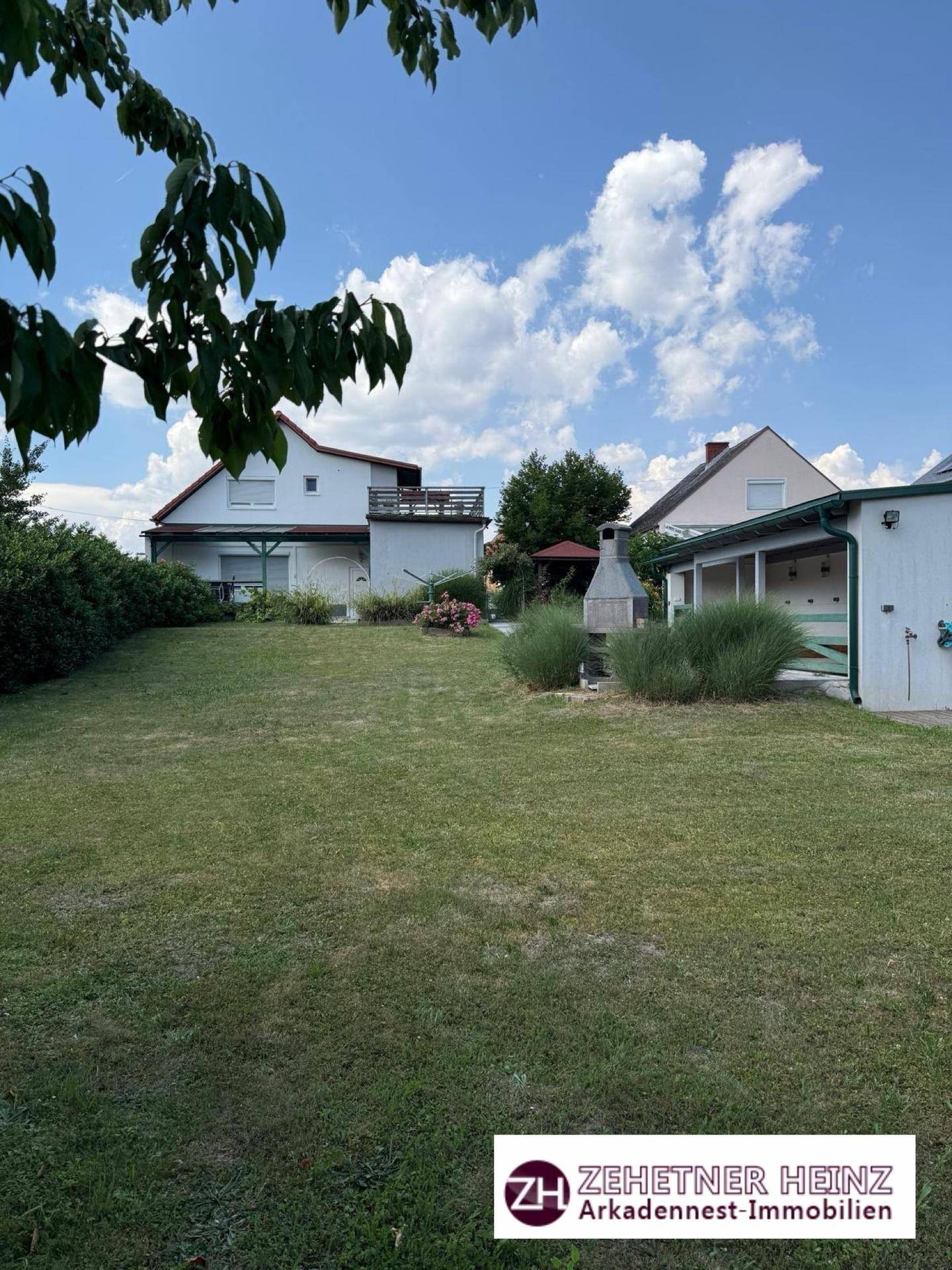 Weitläufiger Rasenbereich des Gartens mit zwei Häusern und einem Grillplatz im Hintergrund.