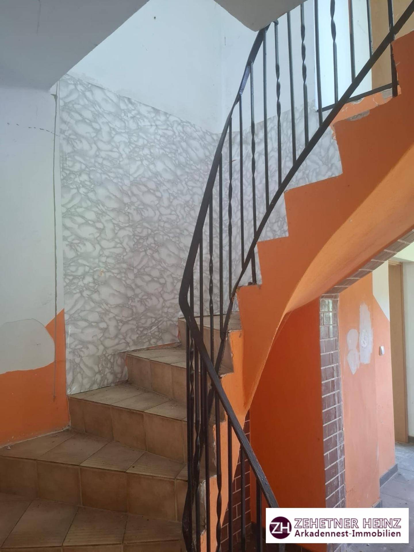 Treppenhaus mit orange gestrichenen Wänden und einem schwarzen Metallgeländer, die Stufen sind gefliest.