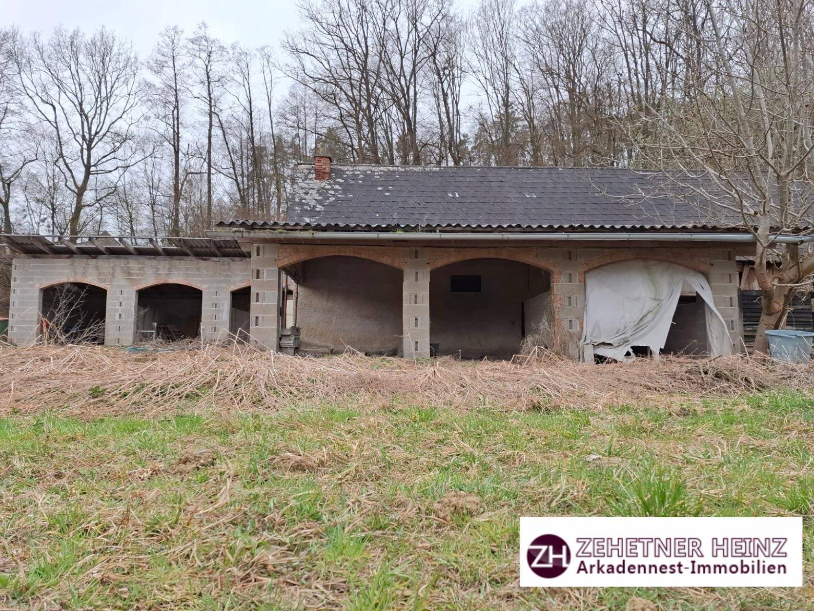 Älteres Nebengebäude mit mehreren Bogenöffnungen und einem Wellblechdach auf einem ländlichen Grundstück.