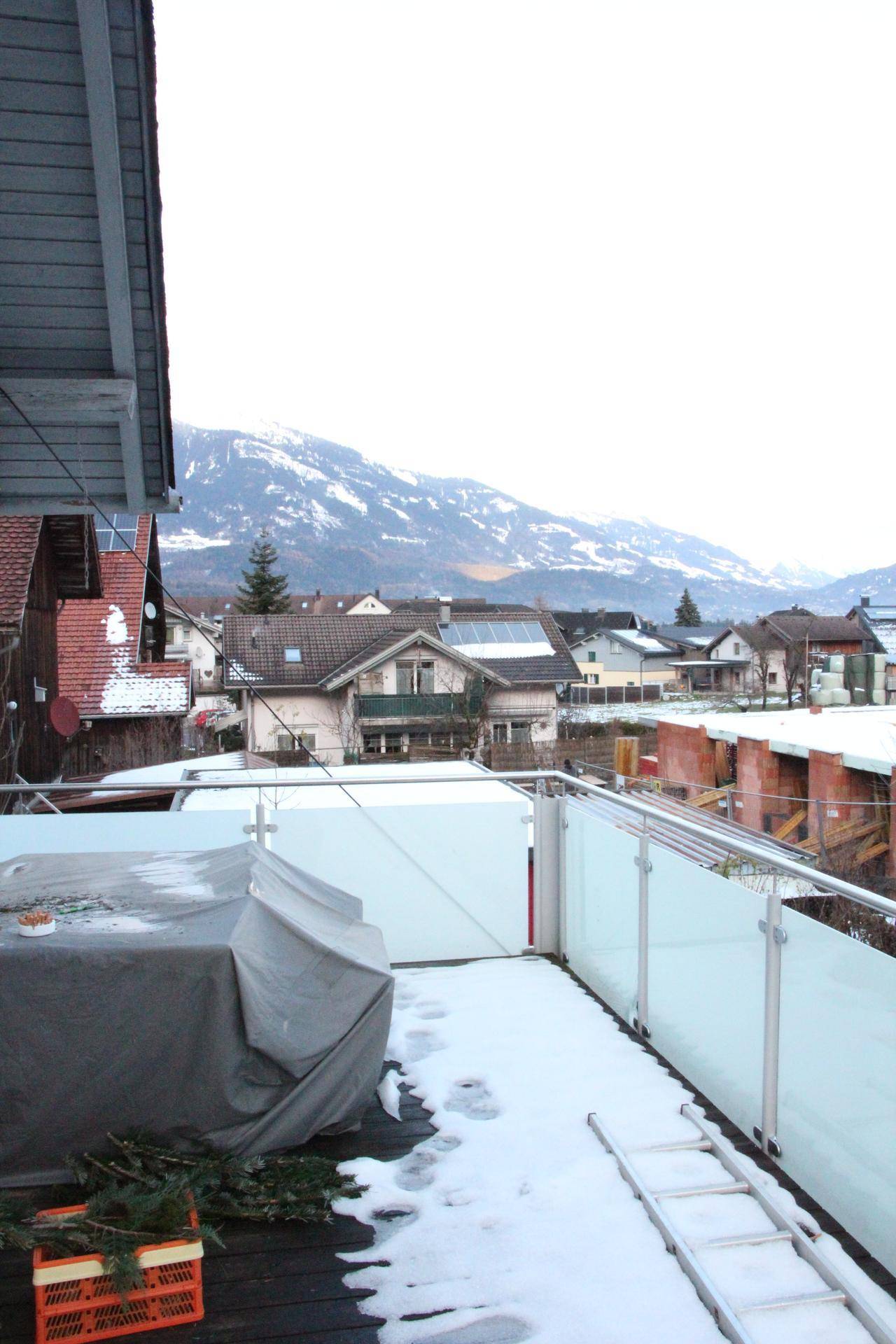 Terrasse mit Schnee und Blick auf die umliegenden Häuser und die schneebedeckten Berge.