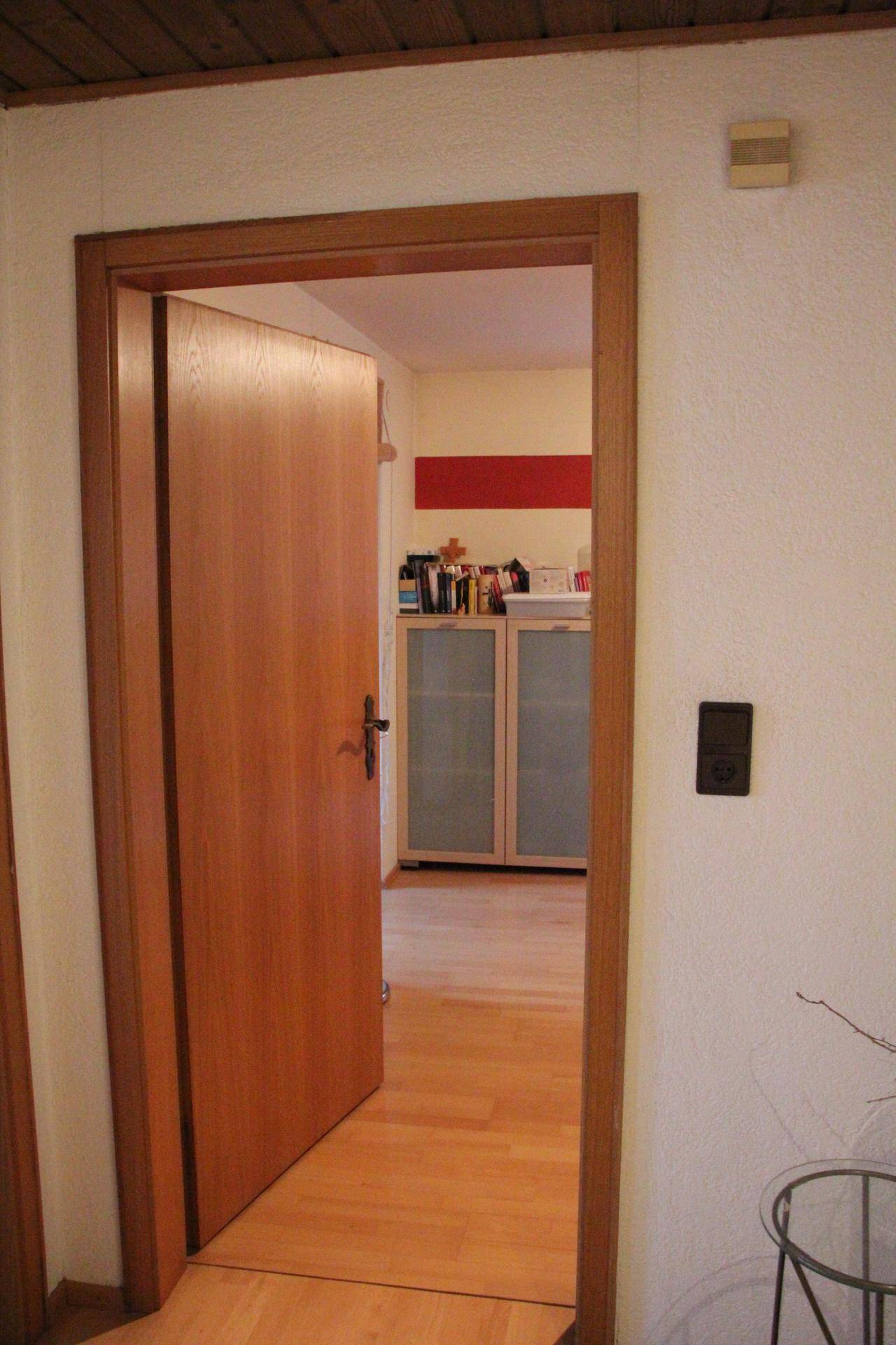 Blick durch eine offene Holztür in einen weiteren Raum mit hellem Holzboden und einem Schrank.