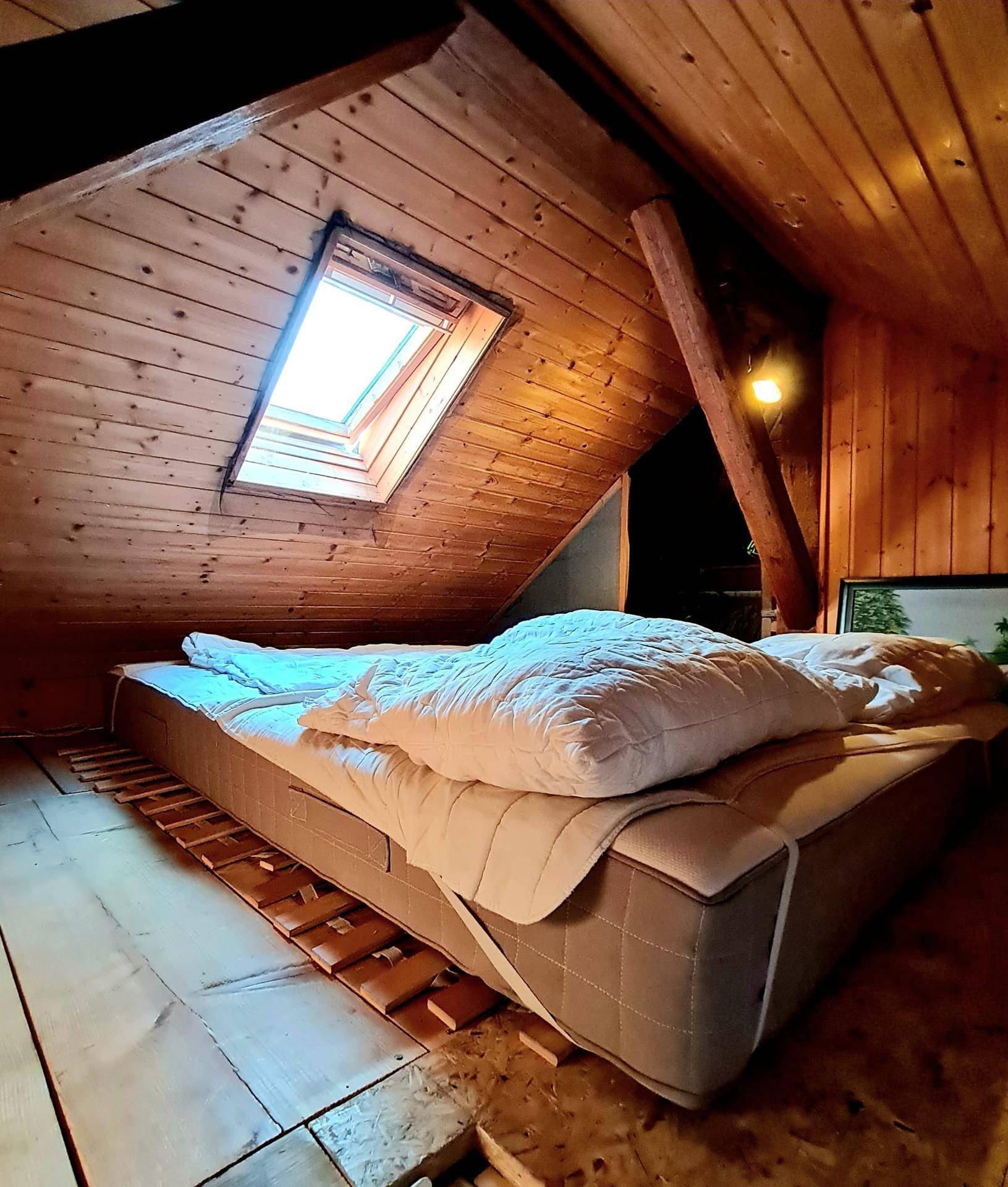 Rustikales Schlafzimmer im Dachgeschoss mit Holzboden, Holzverkleidung und Dachfenster.