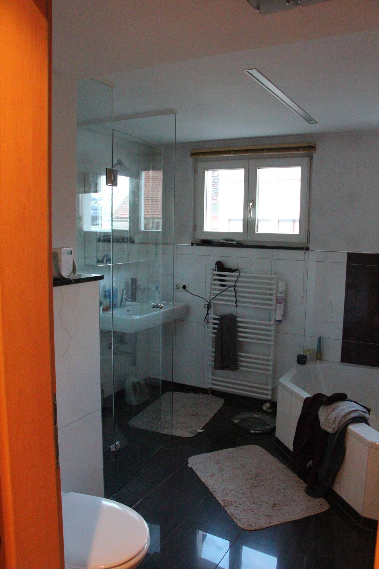 Modernes Badezimmer mit dunklem Fliesenboden, Glasdusche, Badewanne und Fenster für Tageslicht.