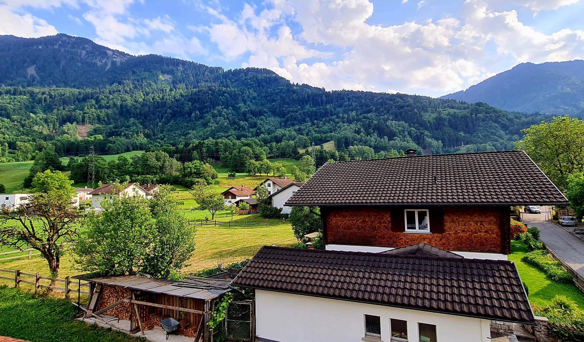Malerischer Blick auf Häuser in einem grünen Tal mit bewaldeten Bergen im Hintergrund.