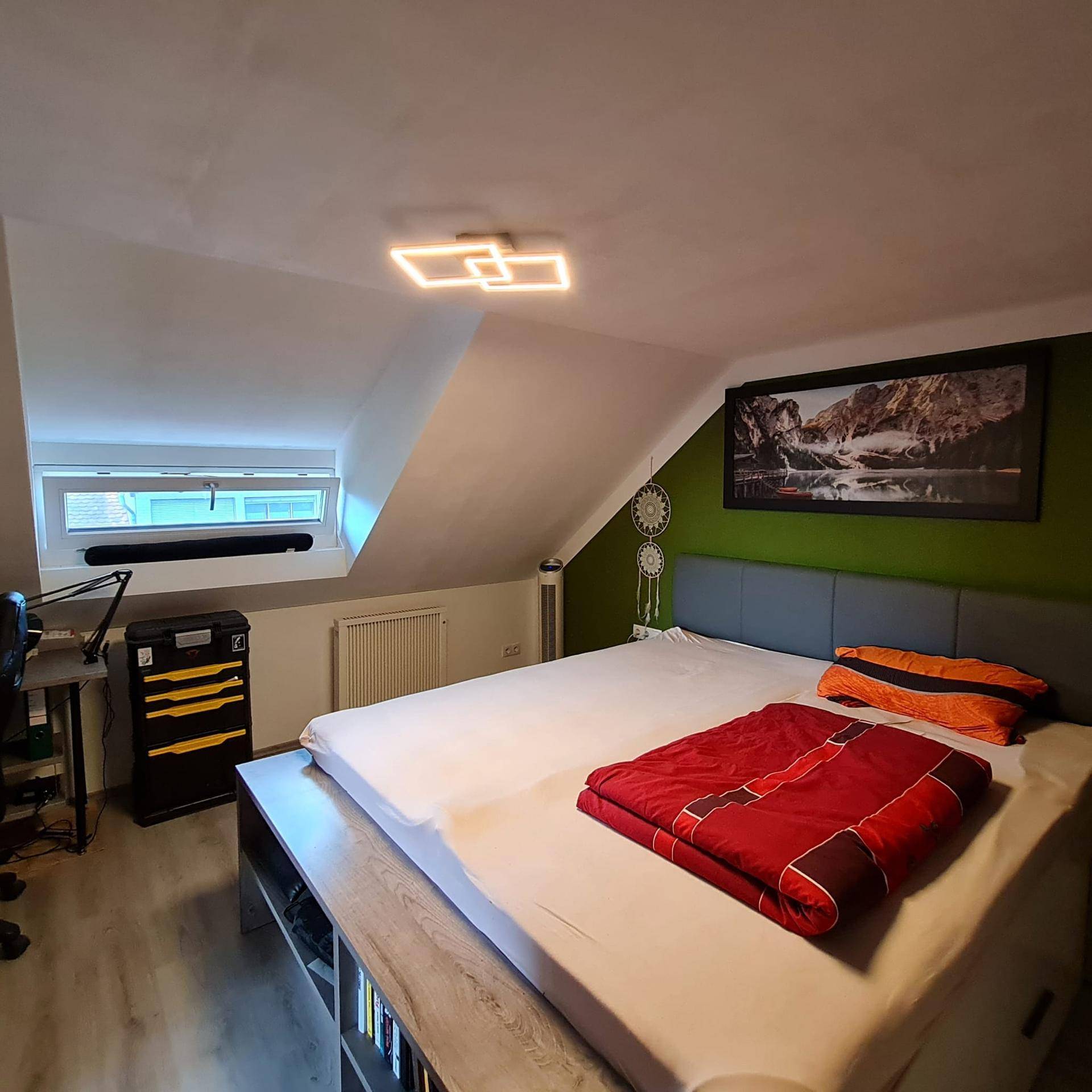 Gemütliches Schlafzimmer im Dachgeschoss mit Bett, Schreibtisch und grüner Akzentwand.