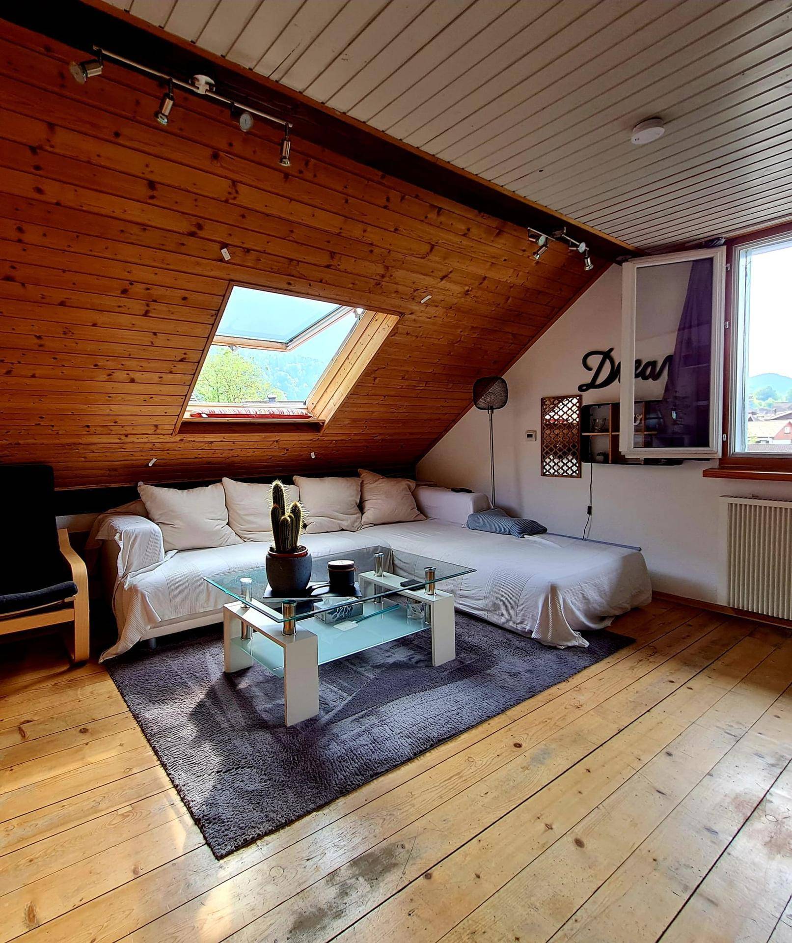 Helles Wohnzimmer im Dachgeschoss mit Sofa, Couchtisch, Holzboden und Dachfenster.
