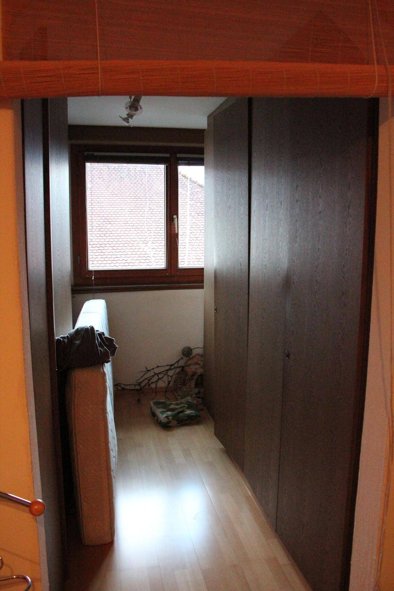 Schmaler Raum mit dunklen Holzschränken und einem Fenster, möglicherweise als Abstellraum genutzt.