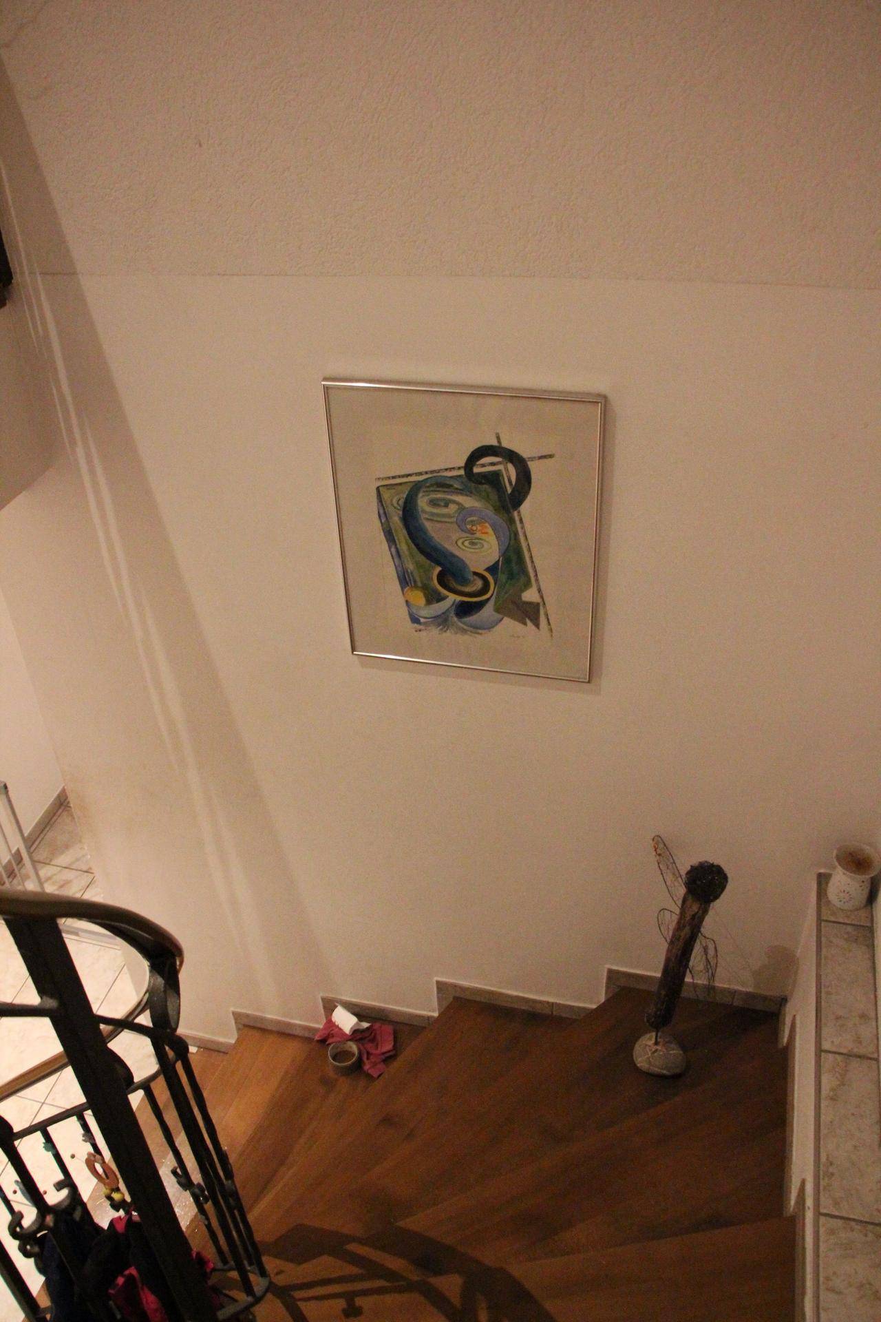 Holztreppe mit Metallgeländer und einem farbigen Kunstwerk an der Wand, führt in die obere Etage.
