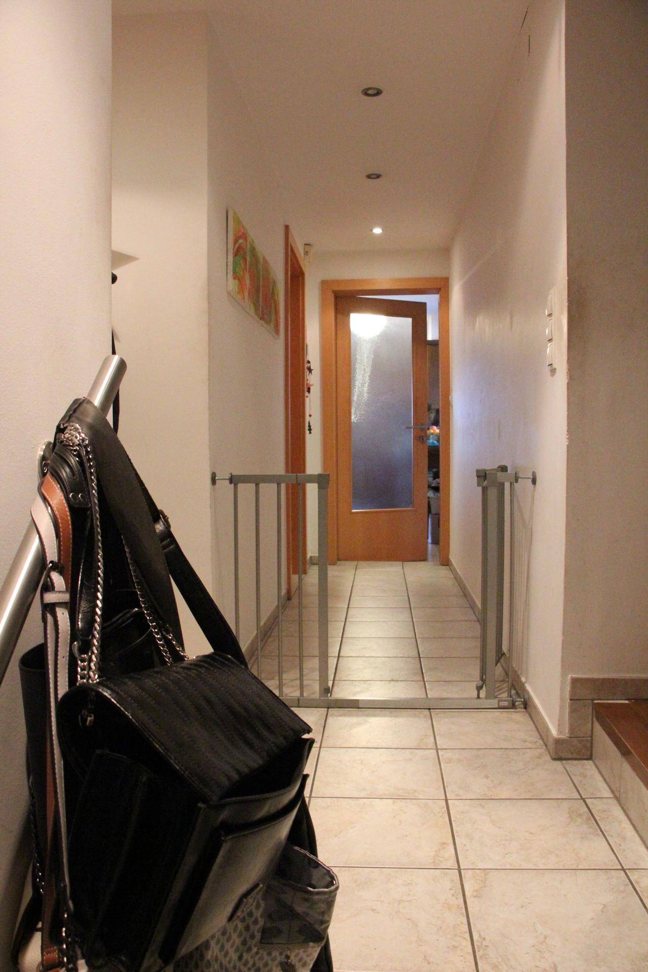 Langer Flur mit Fliesenboden und Holztür, ausgestattet mit zwei Kinderschutzgittern für Sicherheit.