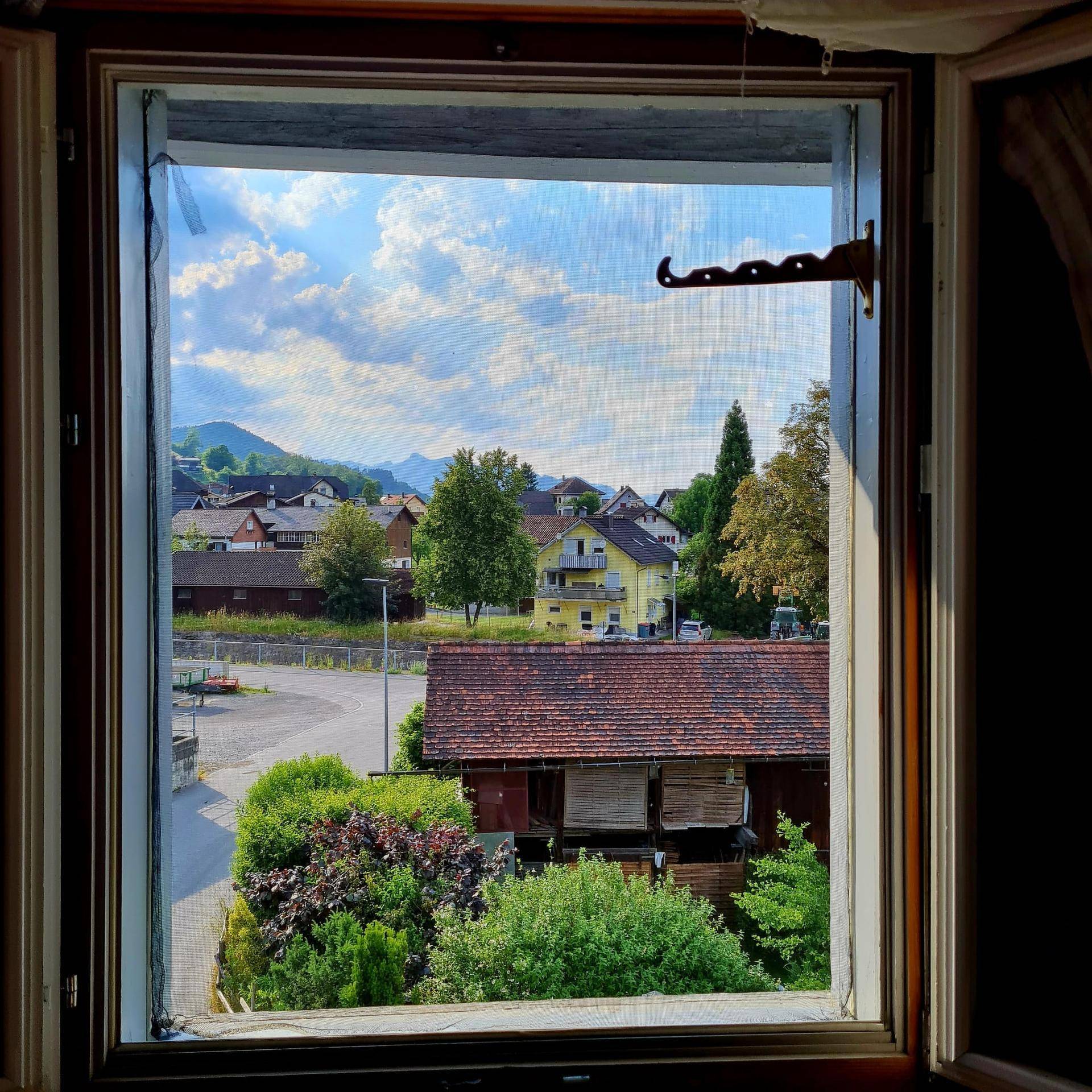 Ausblick aus dem Fenster auf ein Dorf mit Häusern und grünen Hügeln.