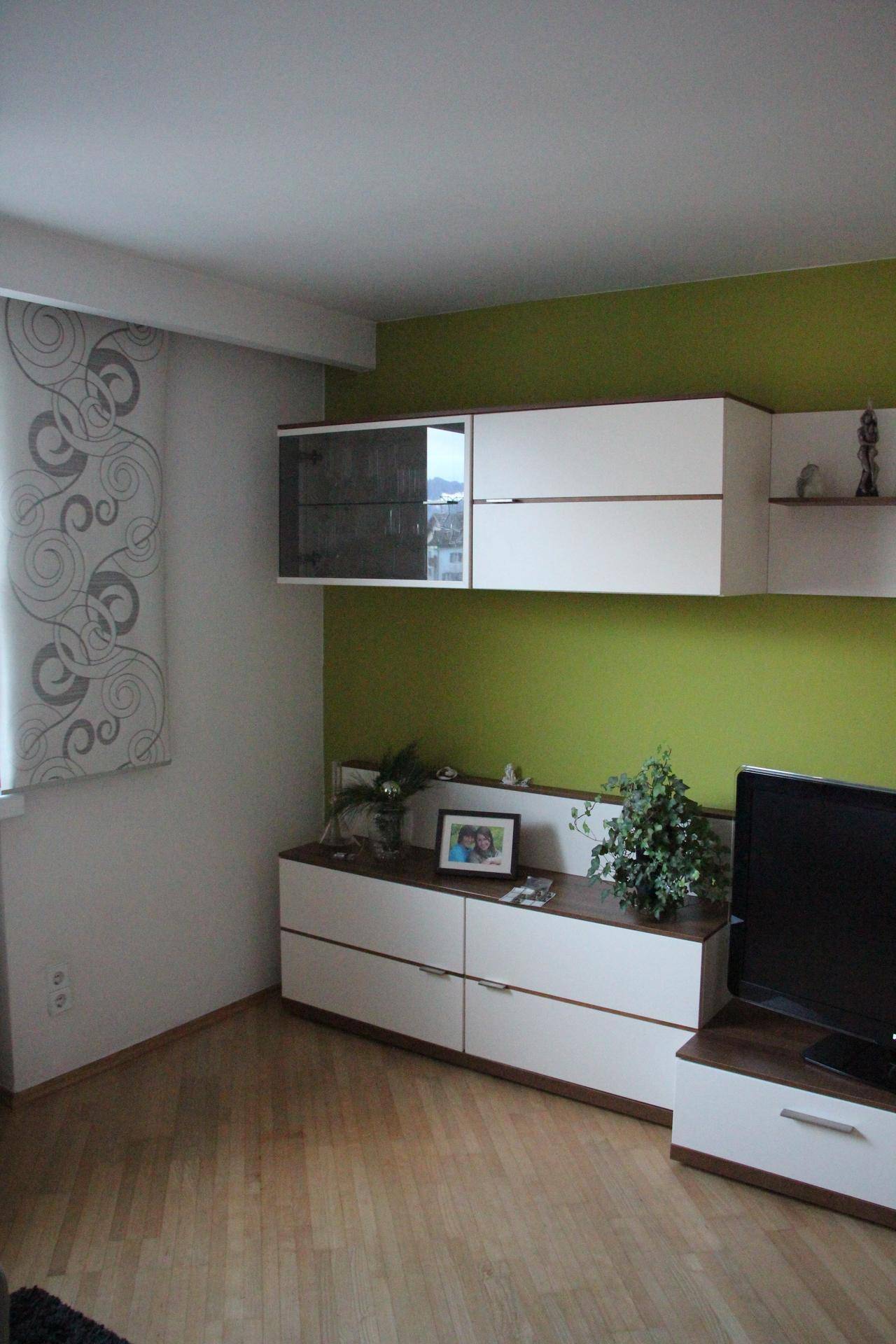 Helles Wohnzimmer mit Laminatboden, einer grünen Akzentwand und modernen weißen Möbeln.