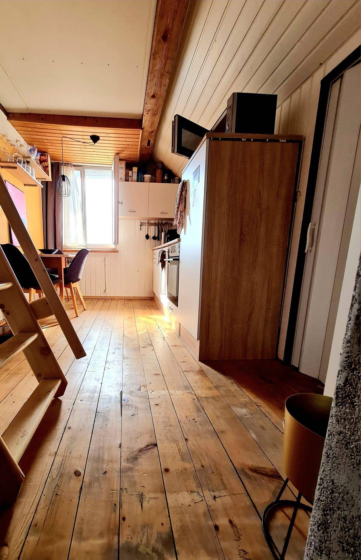 Küche im Dachgeschoss mit Holzboden, weißen Schränken und einer Leiter zum oberen Bereich.