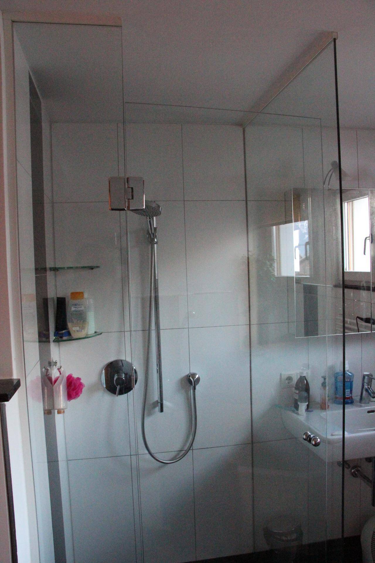 Detaillierte Ansicht einer modernen Dusche mit Glasabtrennung und weißen Wandfliesen im Badezimmer.