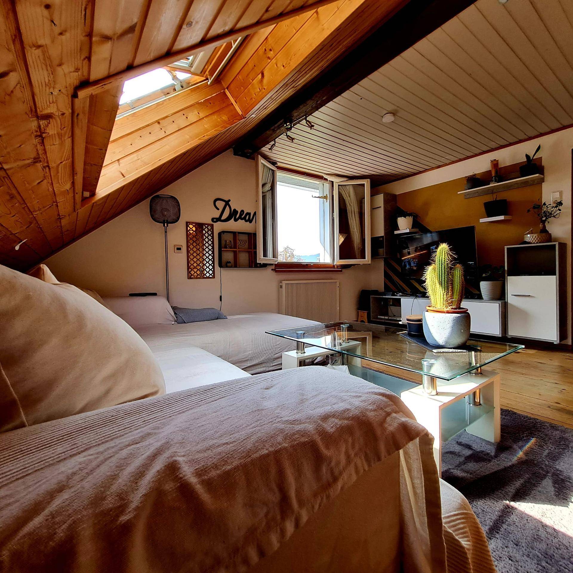 Helles Wohnzimmer im Dachgeschoss mit Sofa, Couchtisch, Holzboden und offenem Fenster.