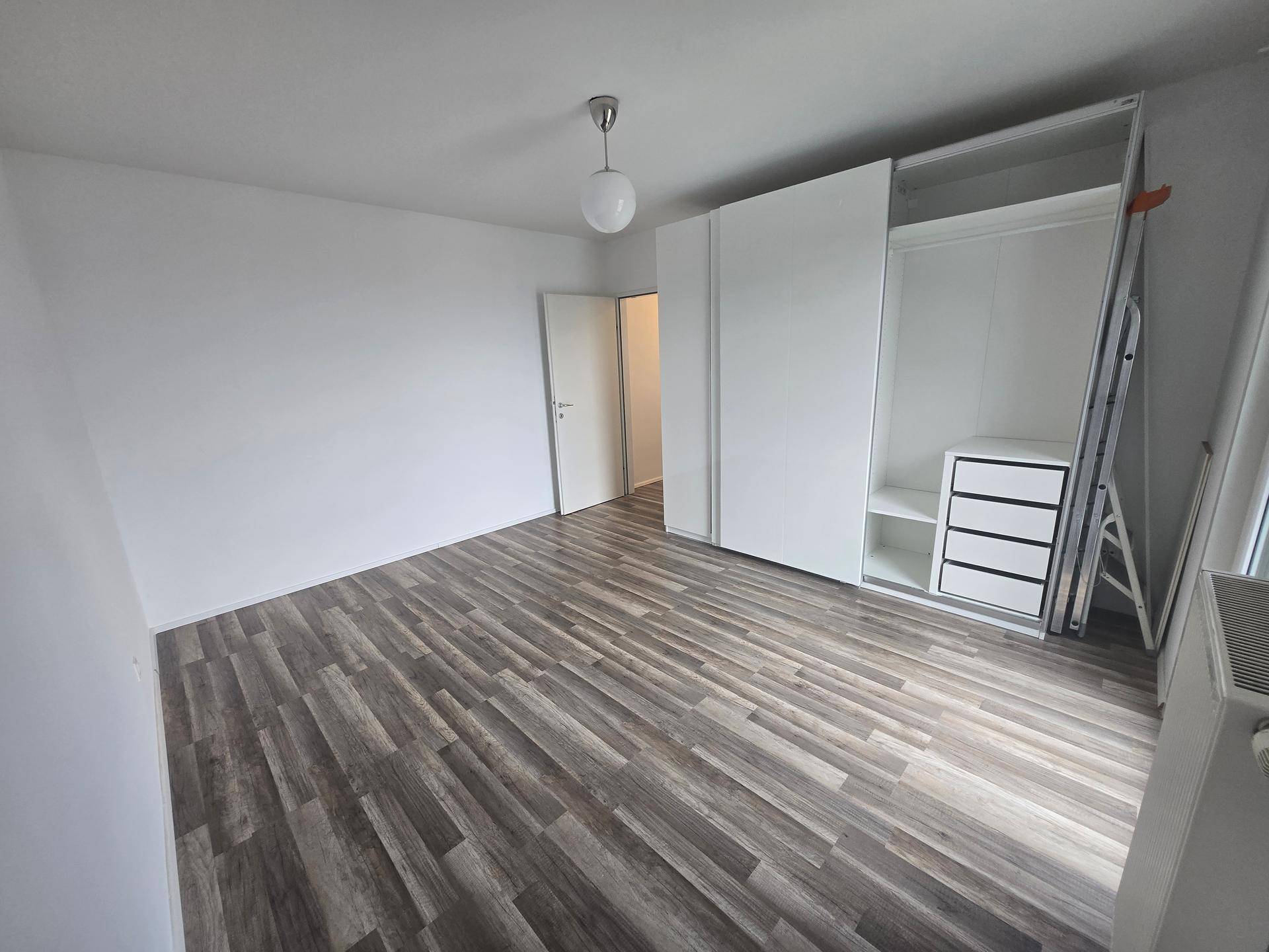 Schlafzimmer mit Laminatboden, weißen Wänden und offenem Kleiderschrank.