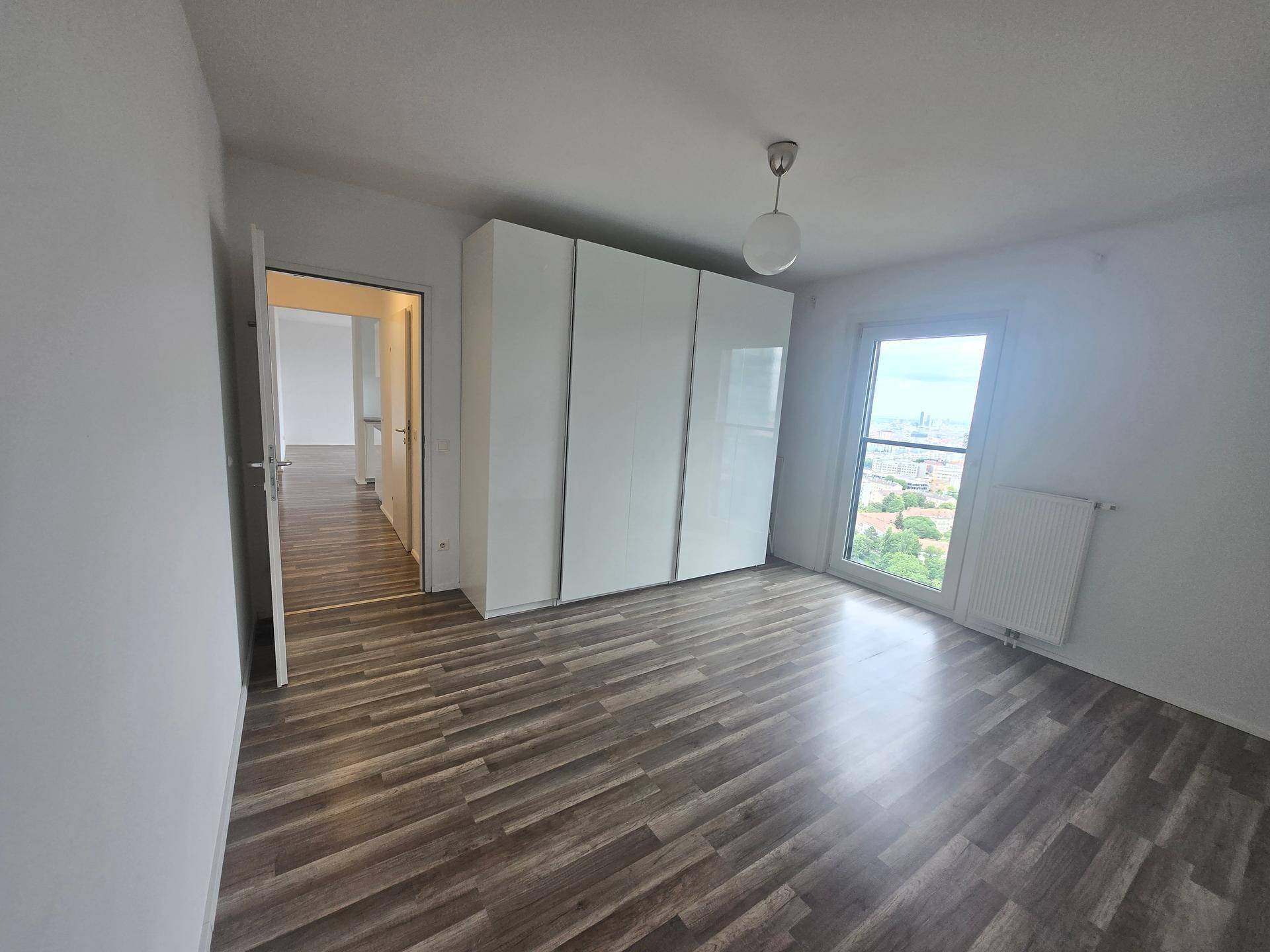 Helles Schlafzimmer mit Laminatboden, großem Kleiderschrank und Fenster mit Stadtblick.