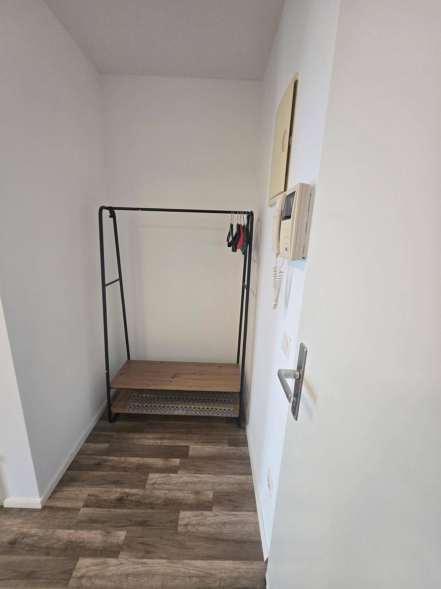 Eingangsbereich mit einfacher Garderobe und Gegensprechanlage auf hellem Laminatboden.