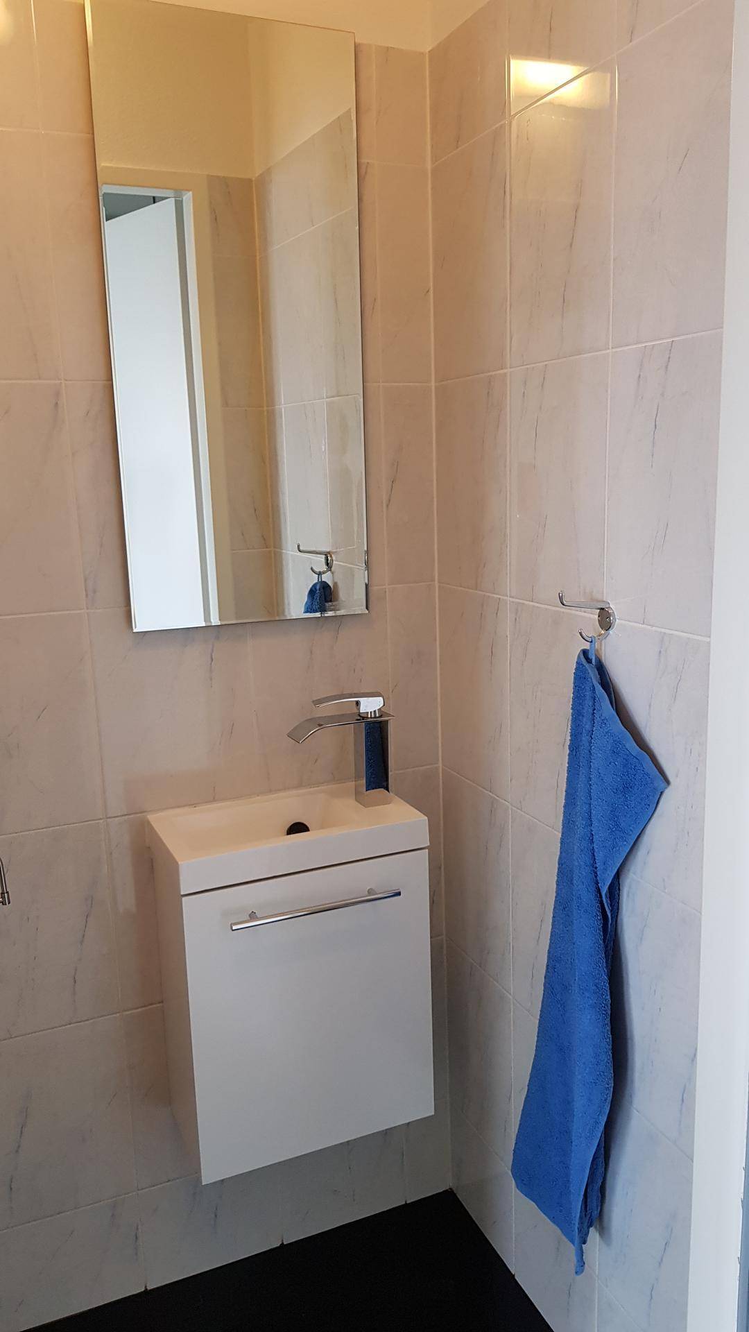 Kleines Gäste-WC mit modernem Waschbecken, Spiegel und hellen Fliesen.