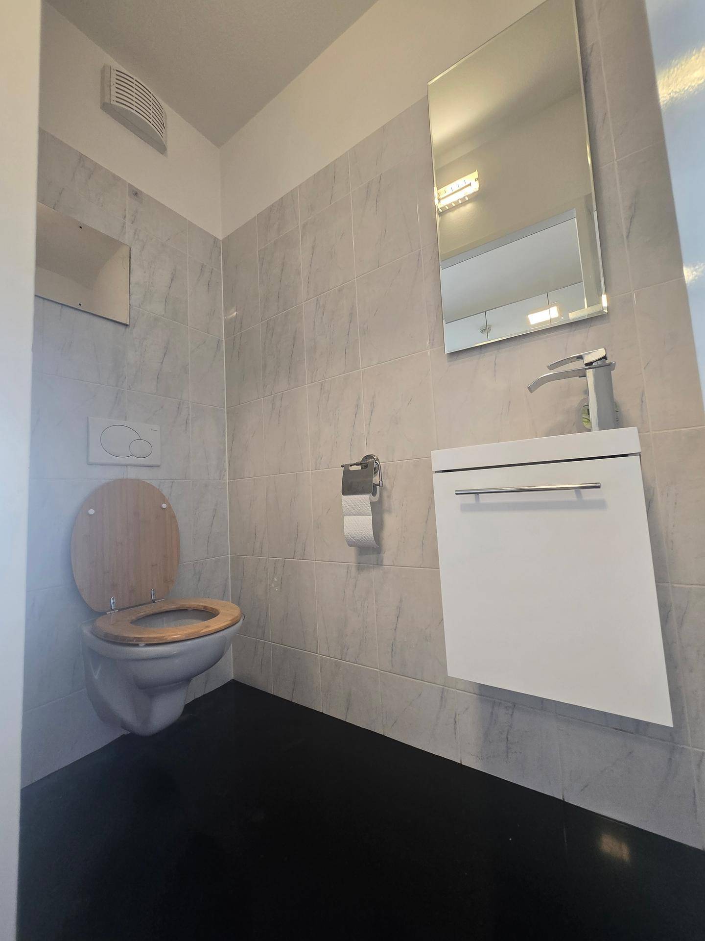 Modernes Gäste-WC mit wandhängender Toilette, kleinem Waschbecken und Spiegel.
