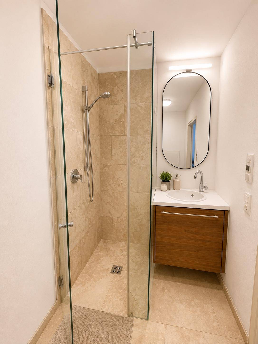 Modernes Badezimmer mit ebenerdiger Dusche, Einzelwaschbecken und hellen Fliesen.