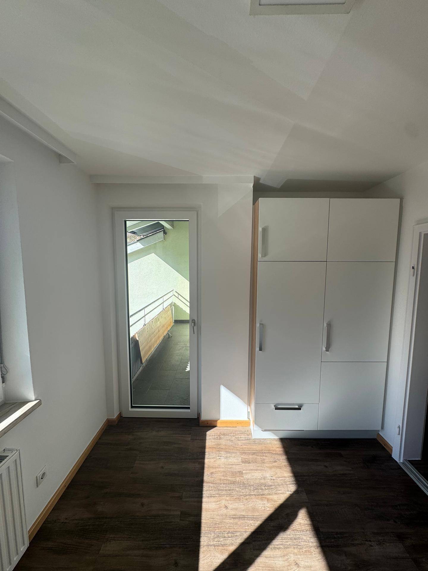 Schlafzimmer mit Einbauschrank, Laminatboden und direktem Zugang zu einem sonnigen Balkon.