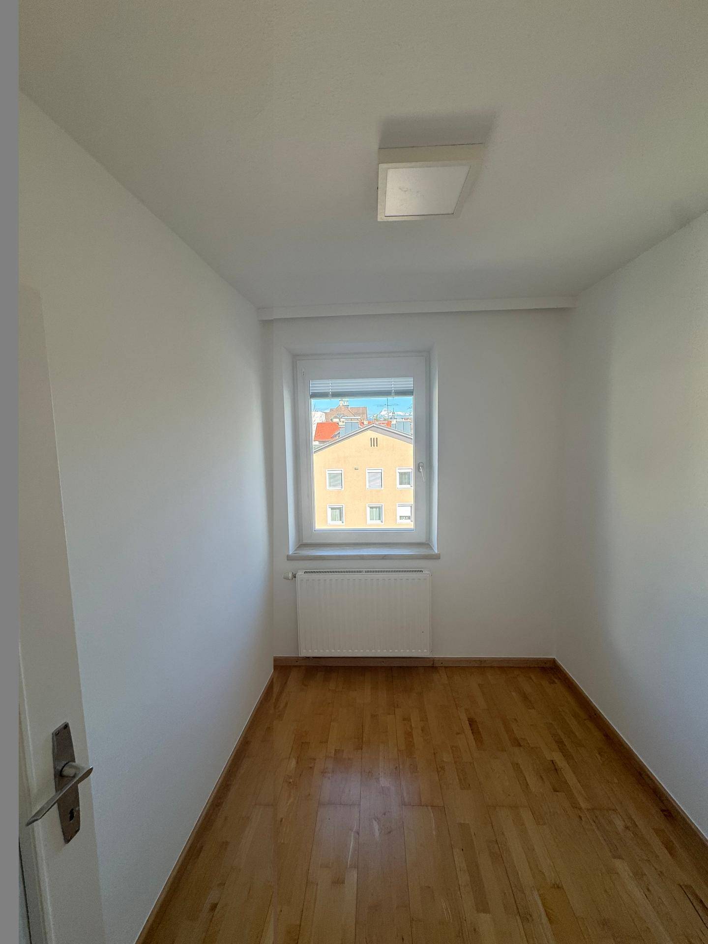 Kleines, helles Zimmer mit Parkettboden und einem Fenster, das eine ruhige Aussicht bietet.