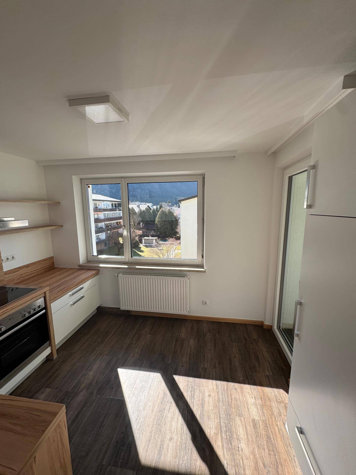Helle Küche mit Holzarbeitsplatten, modernen Schränken und Zugang zu einem Balkon.