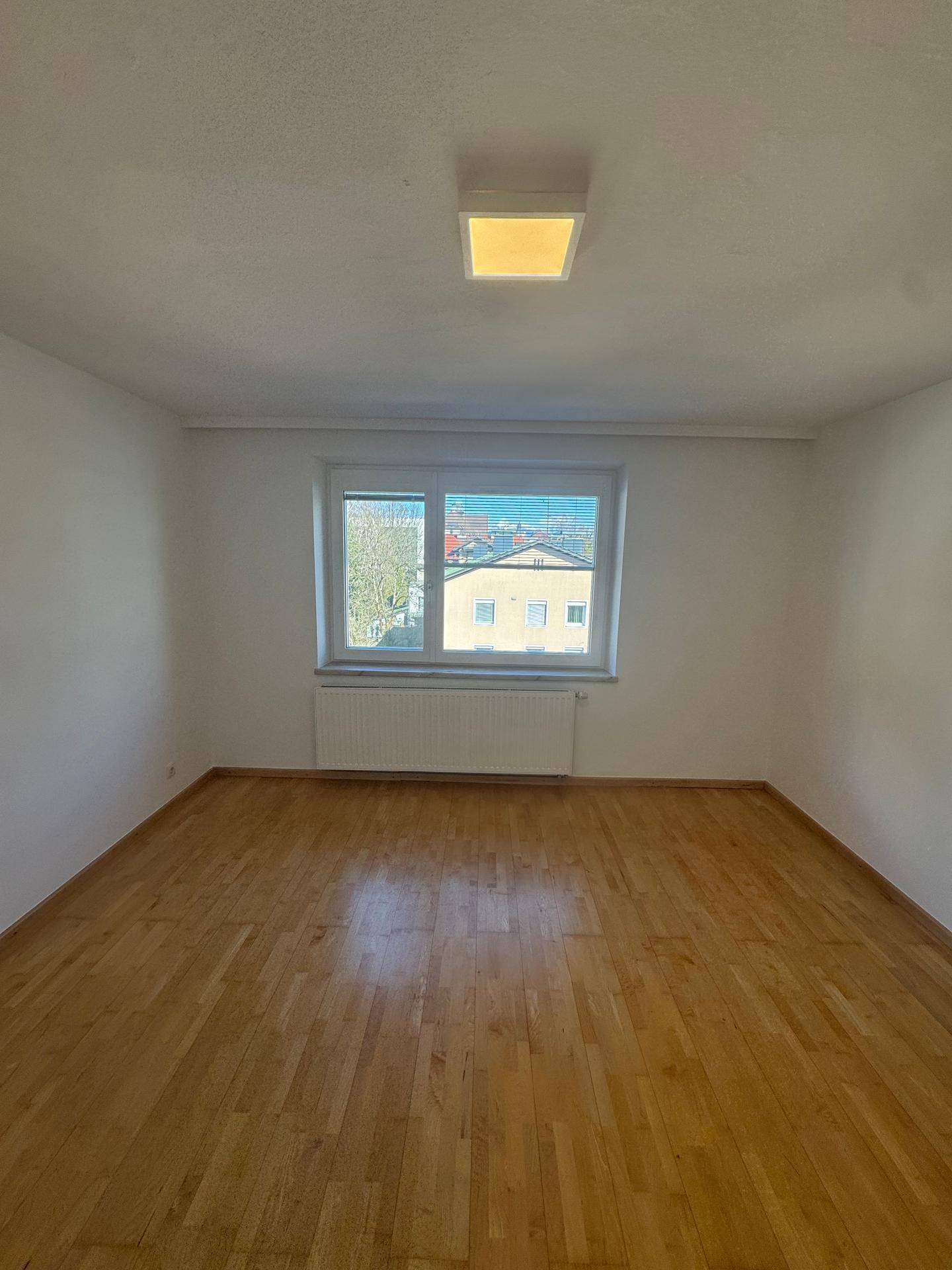 Geräumiges Schlafzimmer mit Holzparkett und einem Fenster, das viel Tageslicht hereinlässt.
