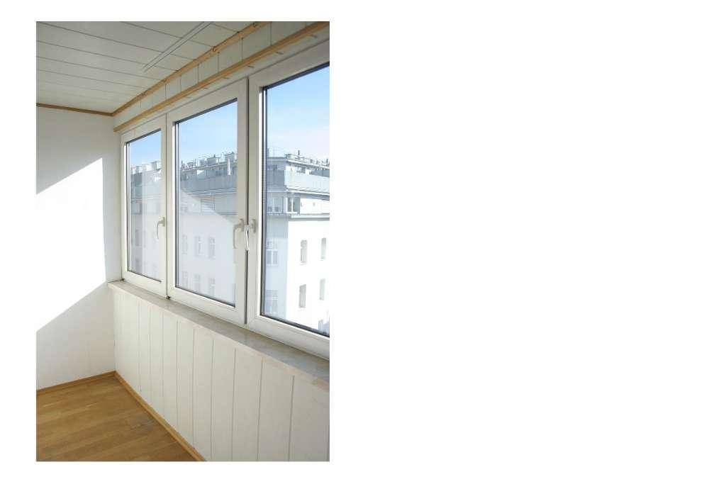 Helle Loggia mit Holzfußboden und großen Fenstern, die einen Blick auf die Stadt bieten.
