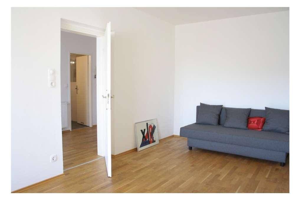 Gemütliches Wohnzimmer mit grauem Sofa, Holzboden und Zugang zu weiteren Räumen.