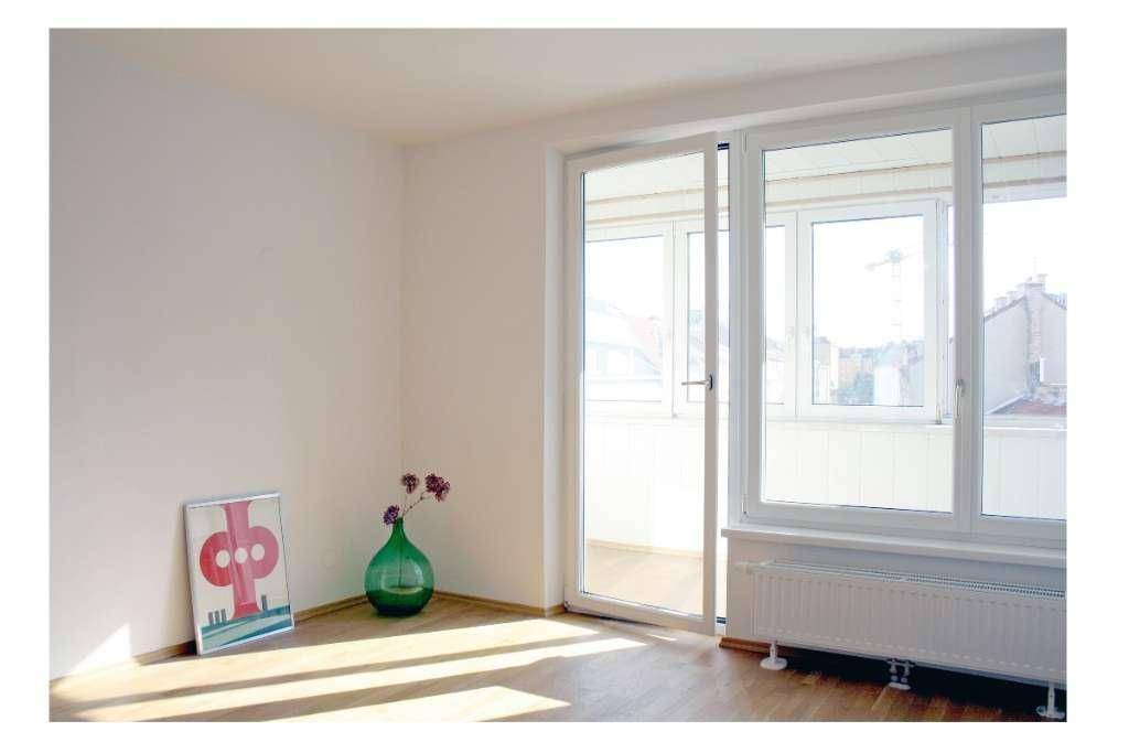 Lichtdurchfluteter Raum mit Holzboden, großem Fenster und Heizkörper, dekoriert mit einer Vase.