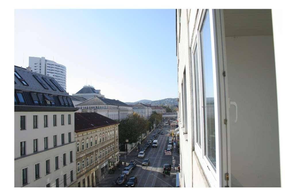 Weitblick über eine belebte Stadtstraße mit Gebäuden und Fahrzeugen unter klarem Himmel.