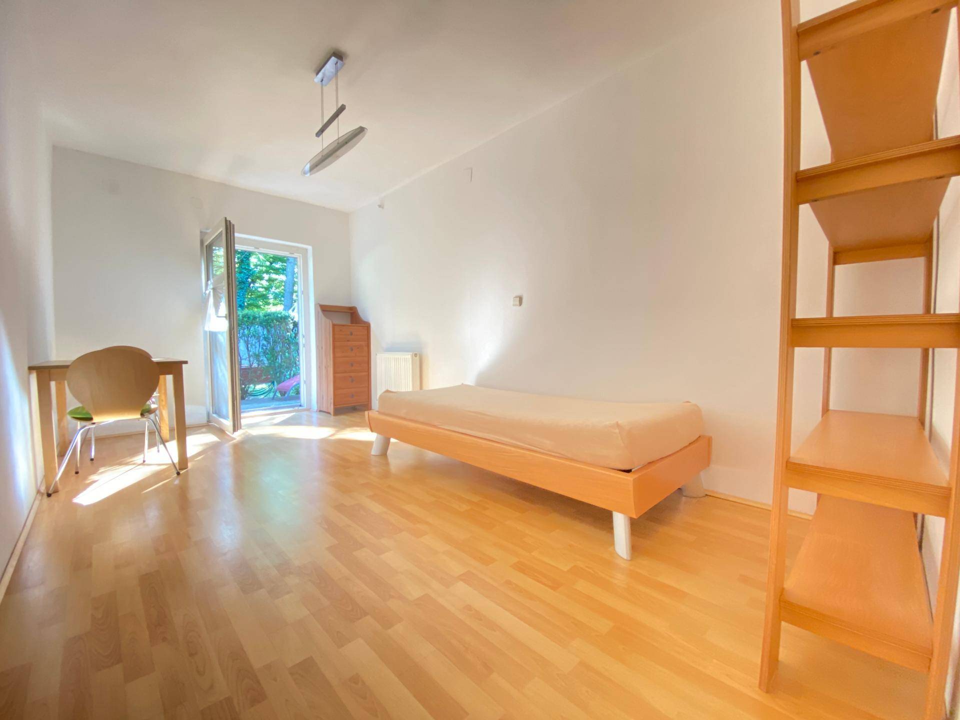 Helles Schlafzimmer mit Holzboden, weiß gestrichenen Wänden und direktem Zugang zum Garten.