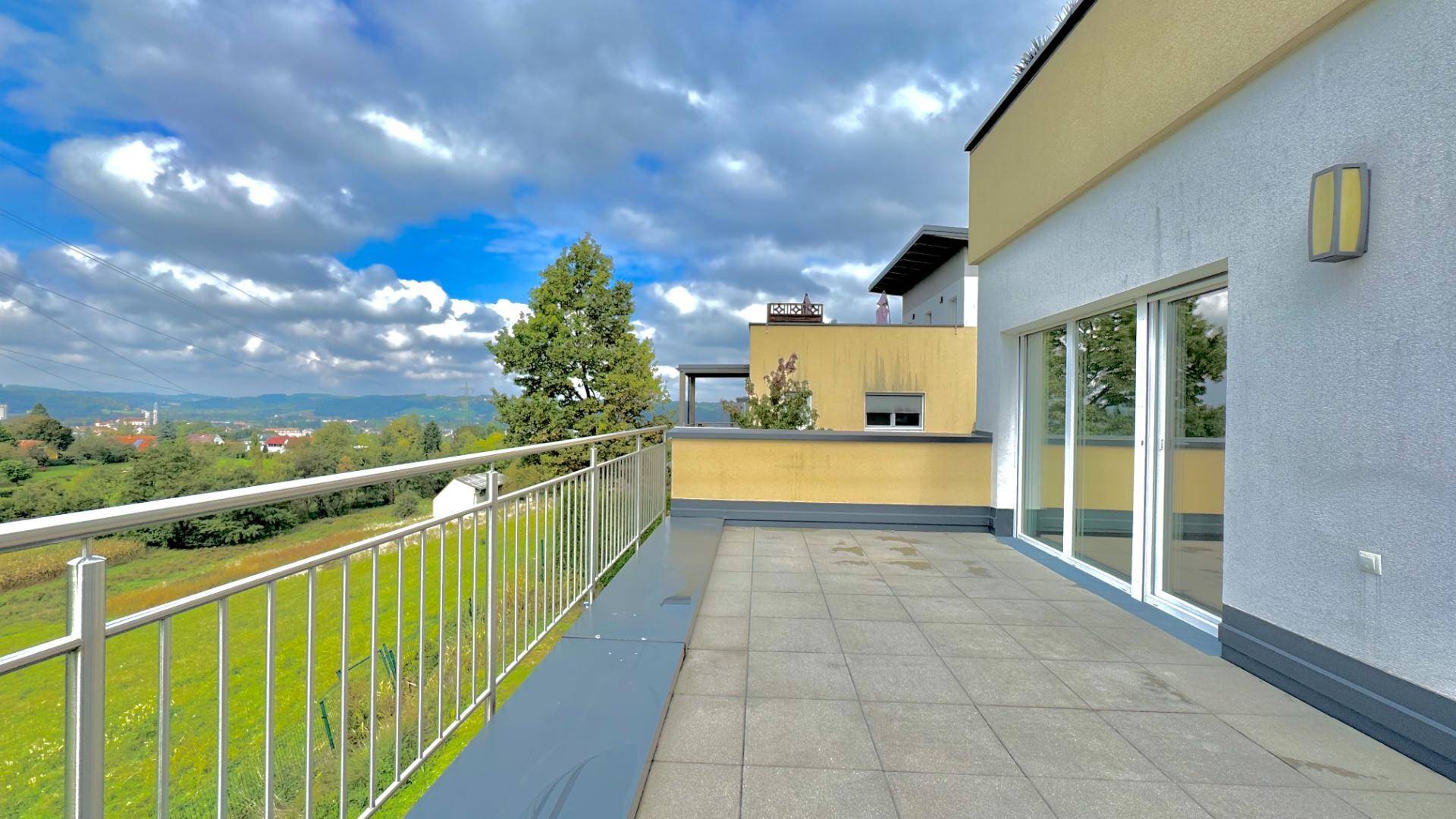 Geräumige Dachterrasse mit Fliesenboden und weitem Blick über die Landschaft und Stadt.