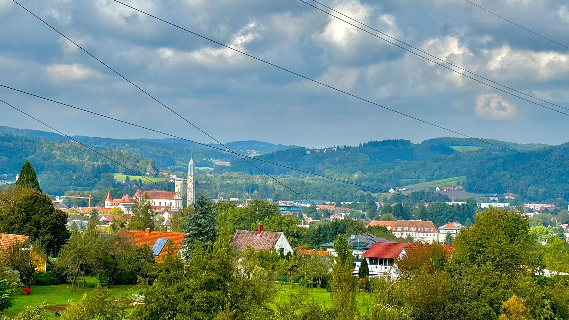 Malerischer Ausblick auf eine ländliche Ortschaft mit Kirche und bewaldeten Bergen.