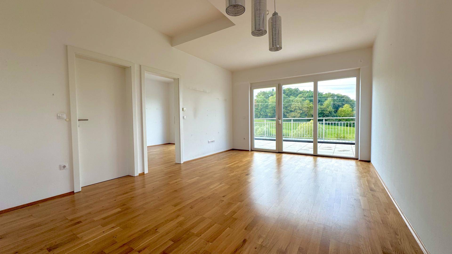 Geräumiges Wohnzimmer mit Holzboden, großen Fenstern und Zugang zur Terrasse.