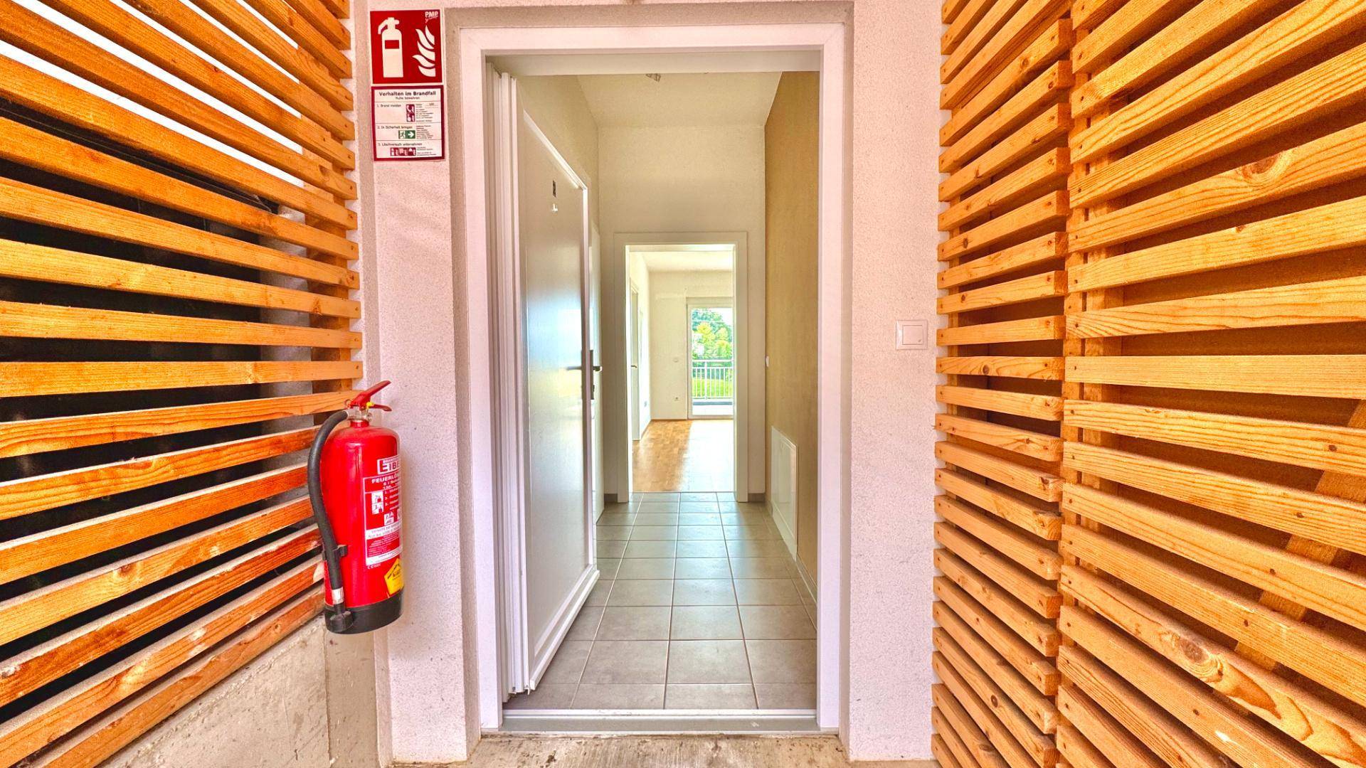 Eingangsbereich mit Holzelementen und Blick in den hellen Flur mit Fliesenboden.