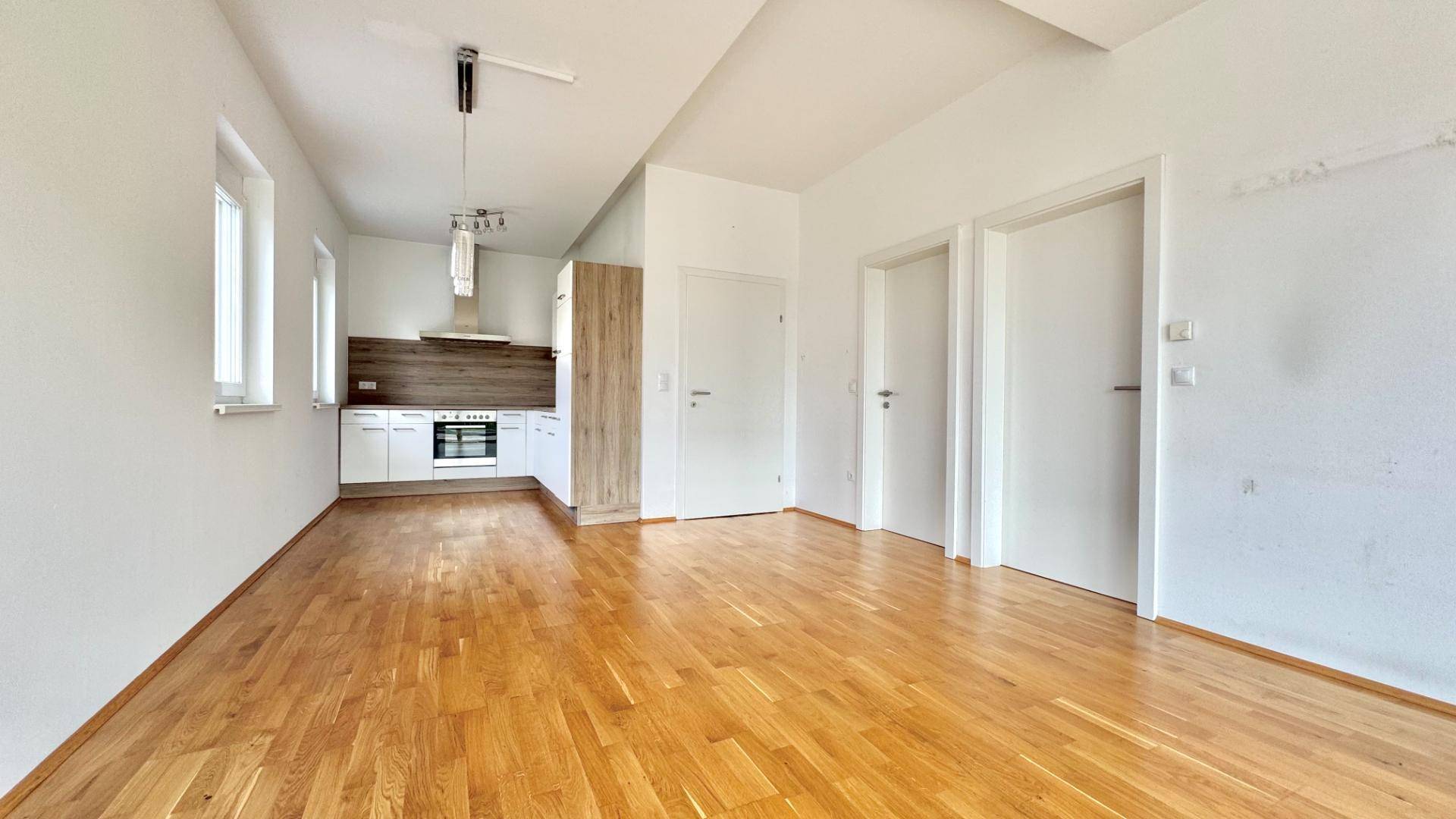 Offener Wohnbereich mit Holzboden und integrierter, moderner Küchenzeile.