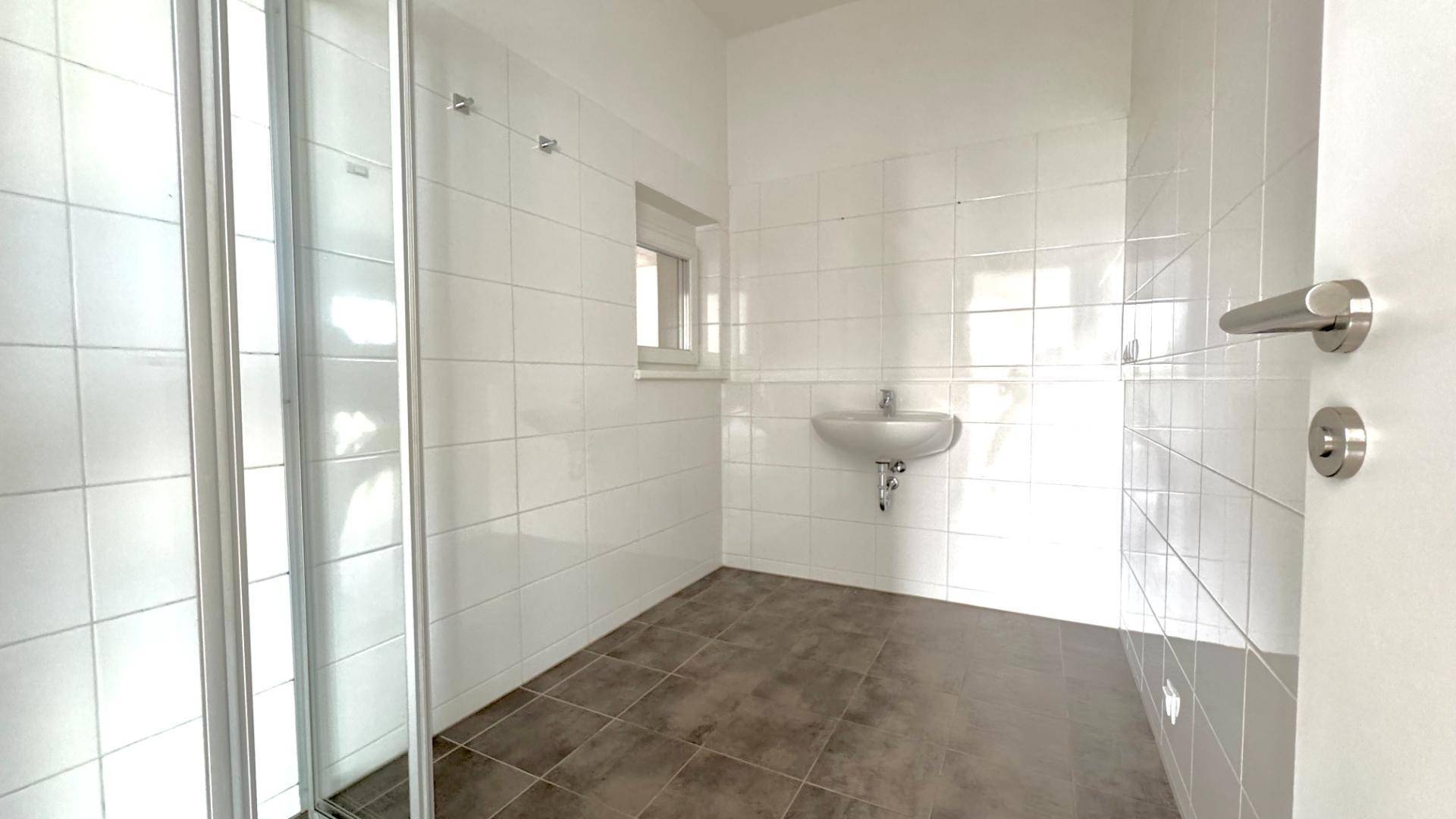 Helles Badezimmer mit Duschkabine, Fliesenboden und Fenster.