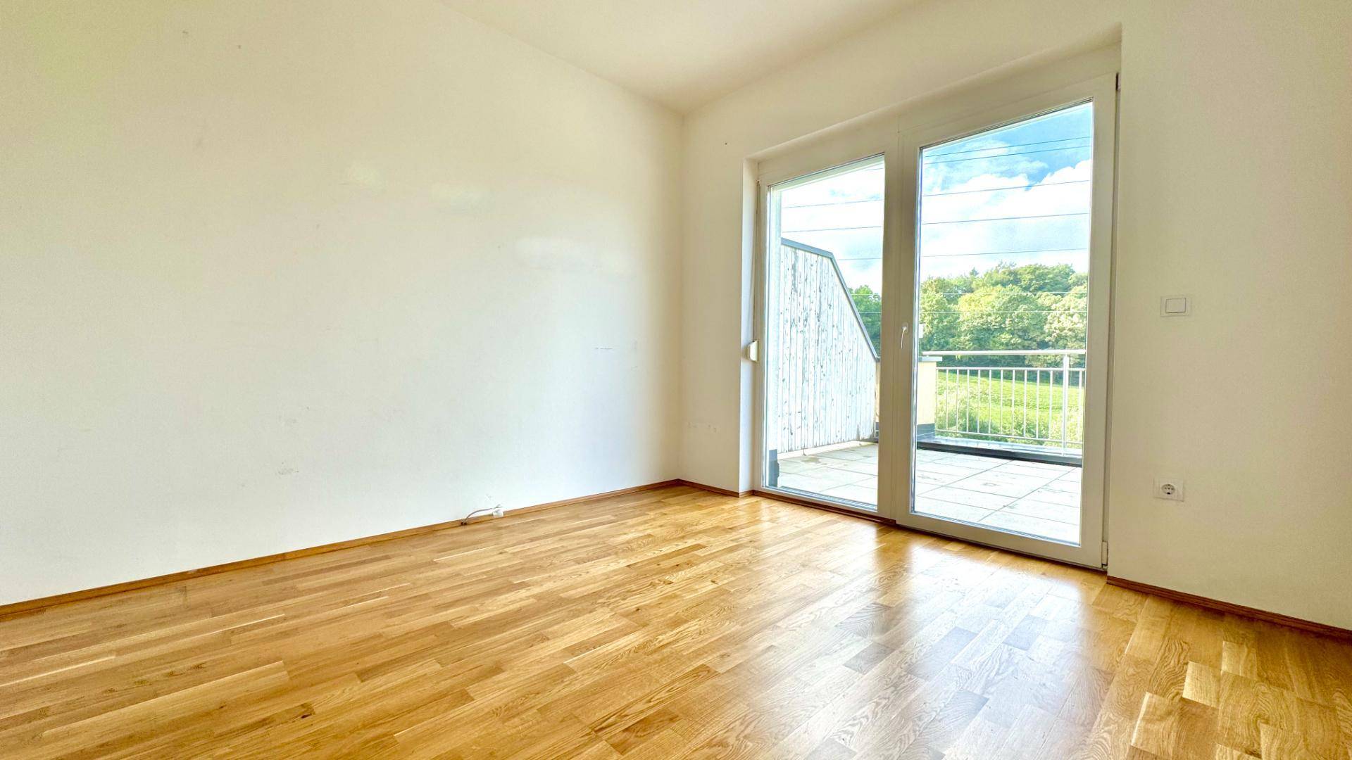 Geräumiges Zimmer mit Holzboden und Zugang zu einer Außenterrasse.