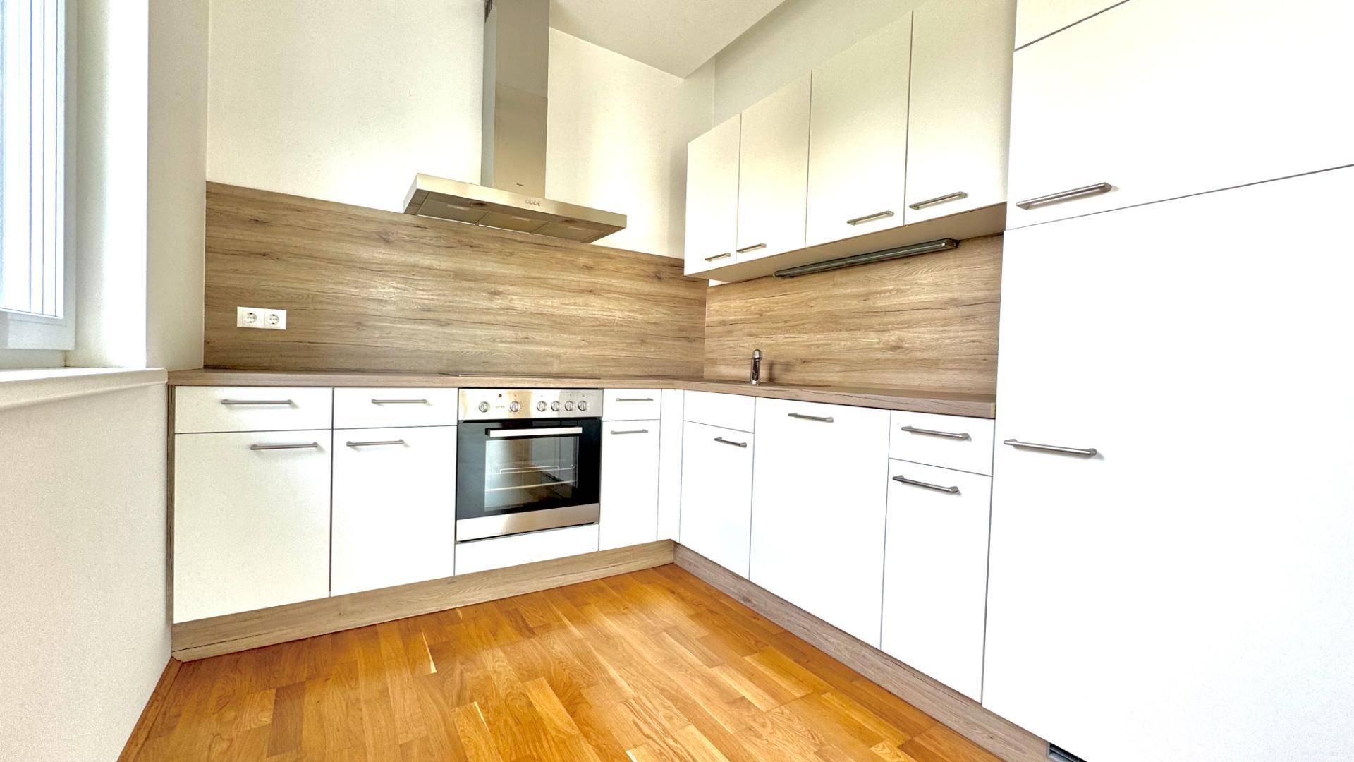 Moderne Küchenzeile mit weißen Schränken, Holzarbeitsplatte und Dunstabzugshaube.