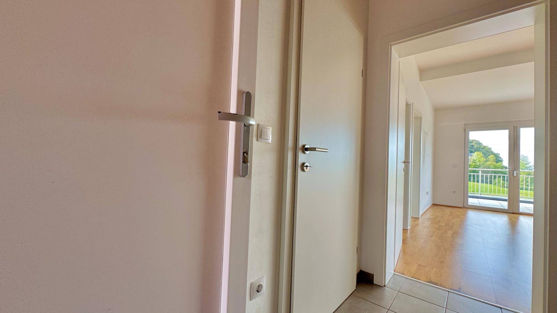 Heller Flur mit Türen und Blick in ein Zimmer mit Holzboden und Balkonzugang.
