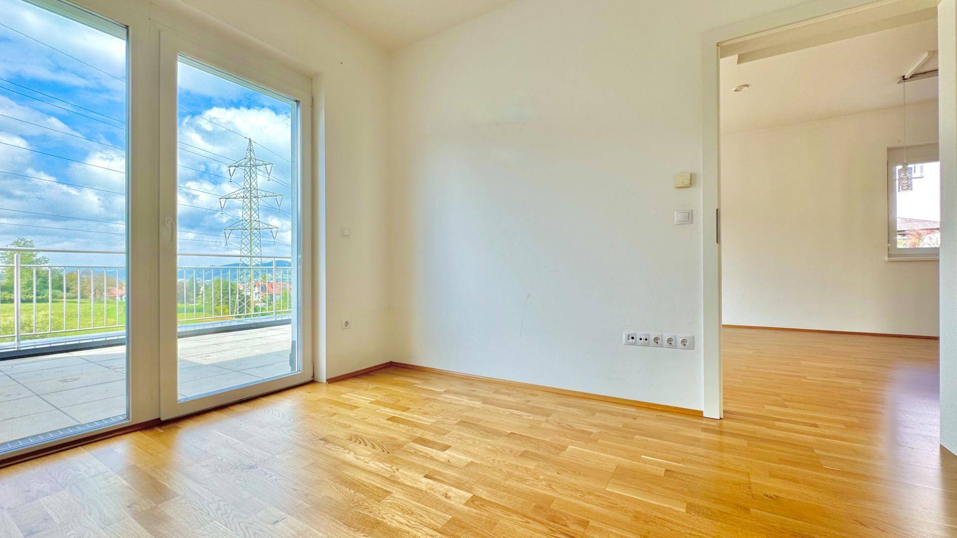 Helles Zimmer mit Holzboden und großem Fenster mit Blick ins Grüne.