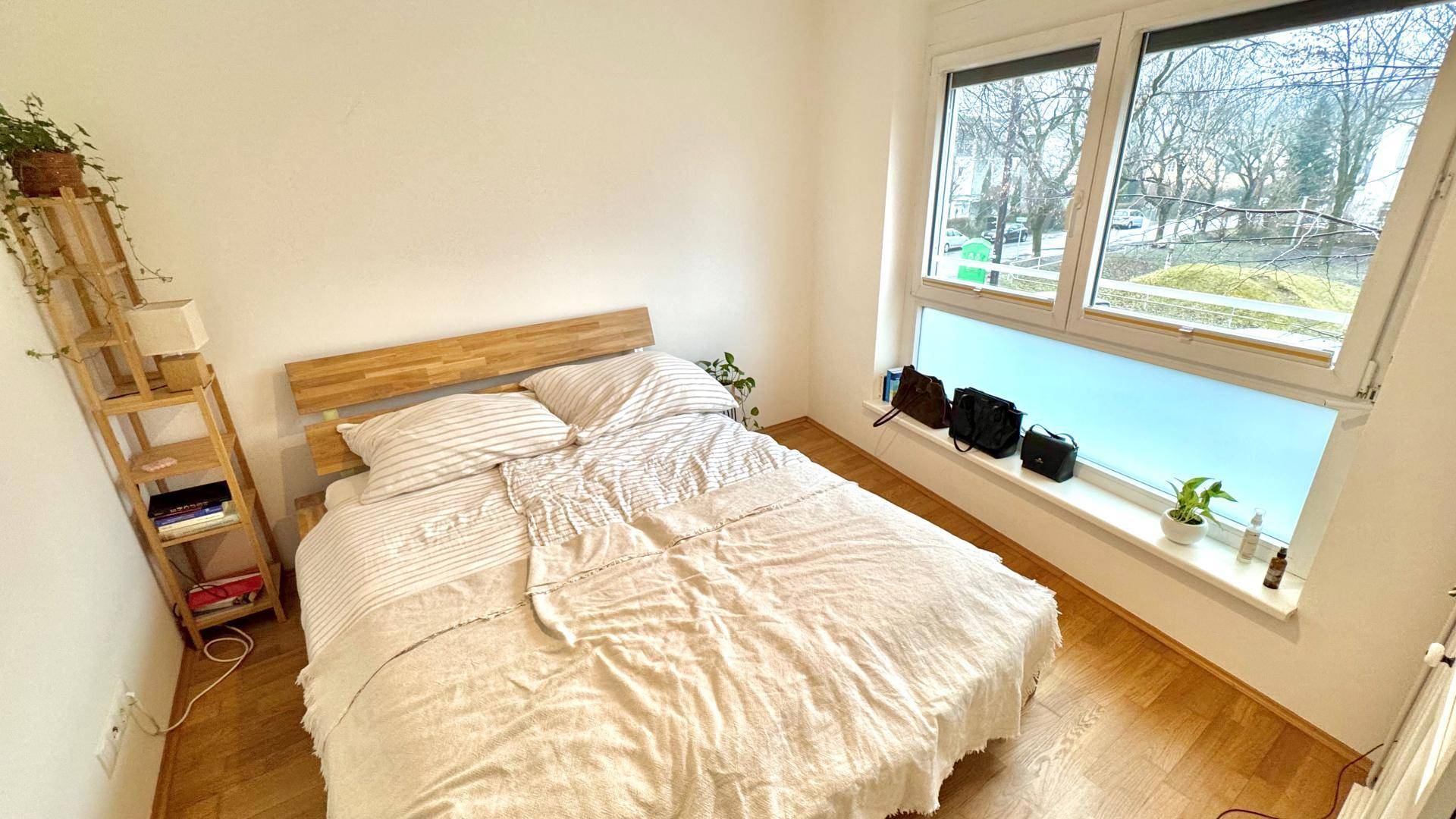 Helles Schlafzimmer mit großem Fenster, Holzbett und Blick ins Grüne, ideal zum Entspannen.