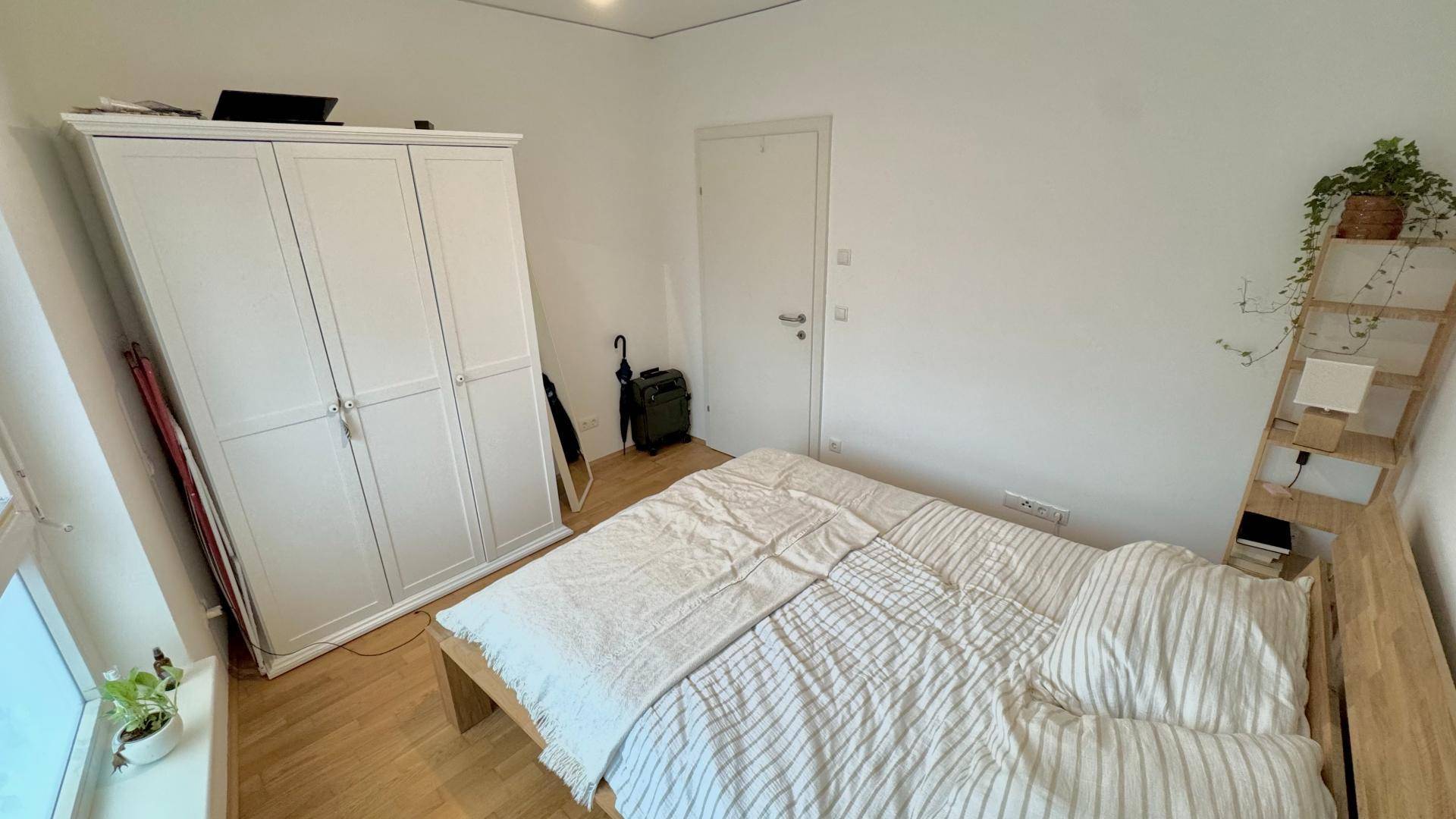 Schlichtes Schlafzimmer mit Holzbett, weißem Kleiderschrank und hellem Holzboden für erholsame Nächte.