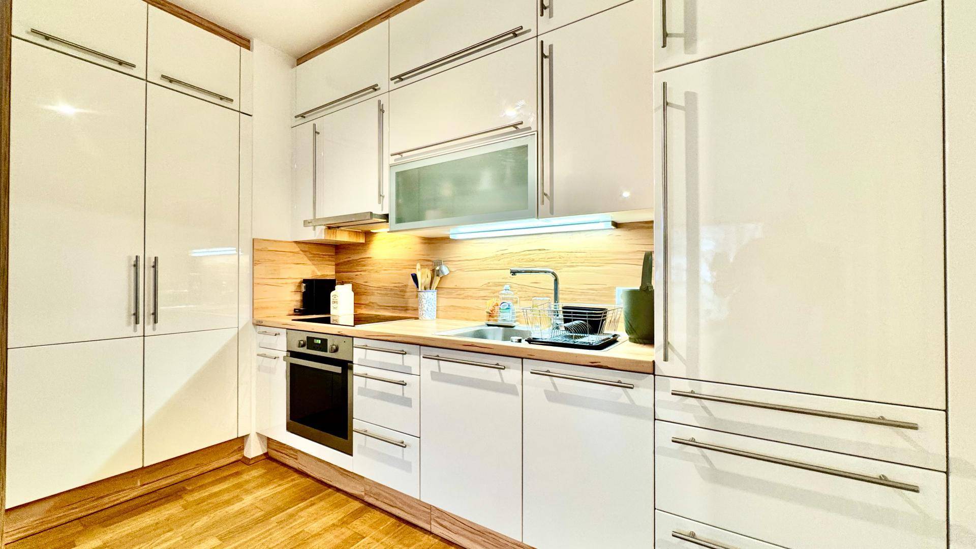 Moderne Einbauküche mit weißen Hochglanzfronten, Holzdetails und integrierten Elektrogeräten.