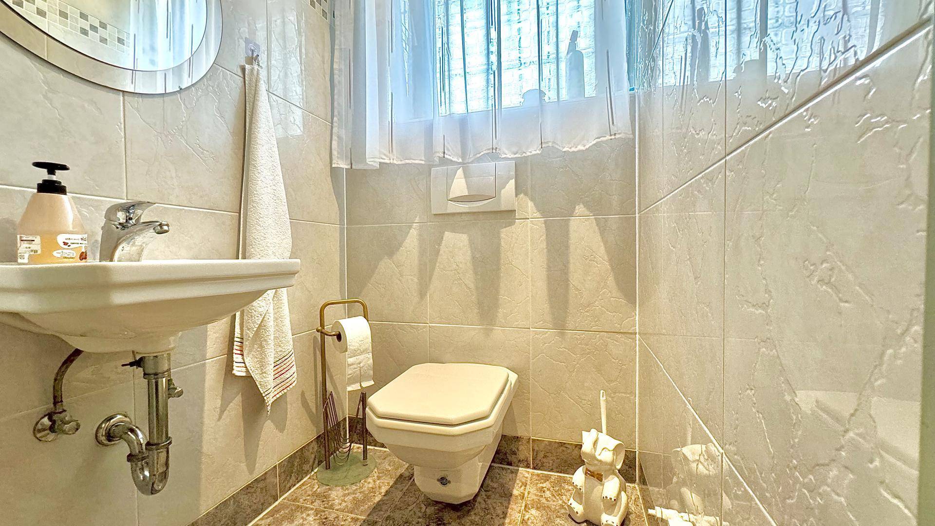 Kleines Gäste-WC mit Waschbecken, Toilette und hellen Fliesen.