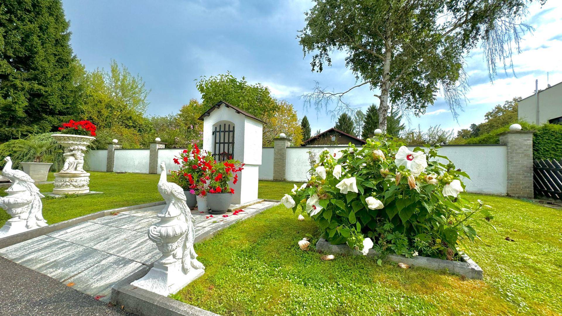 Gartenbereich mit dekorativen Statuen, blühenden Pflanzen und einem kleinen Schrein.